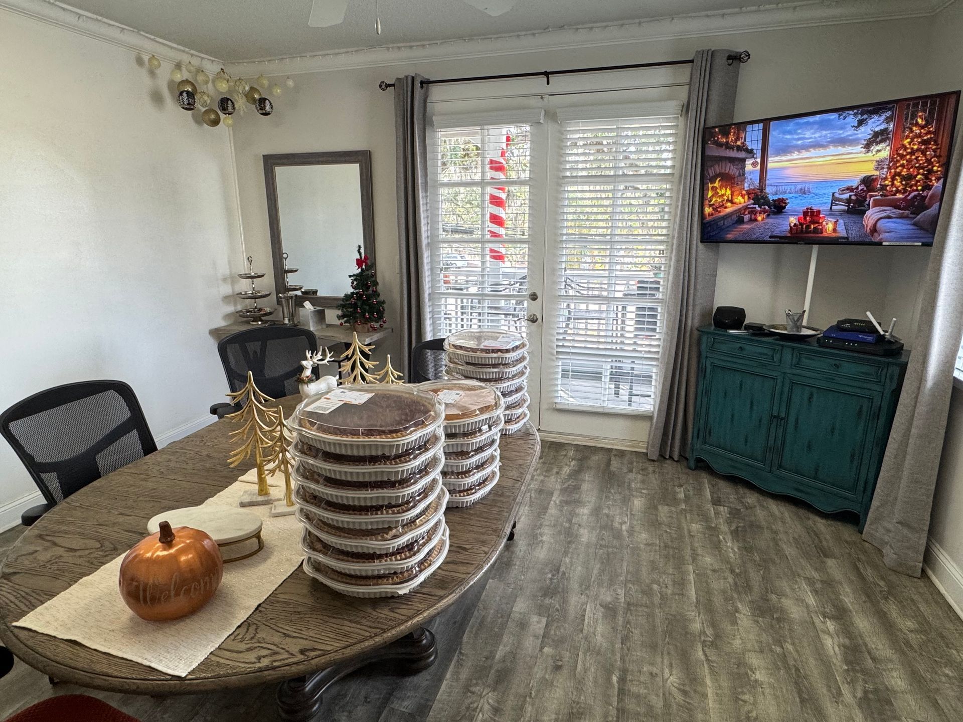 Cozy dining room with round table, stacked plates, teal cabinet, and TV on the wall