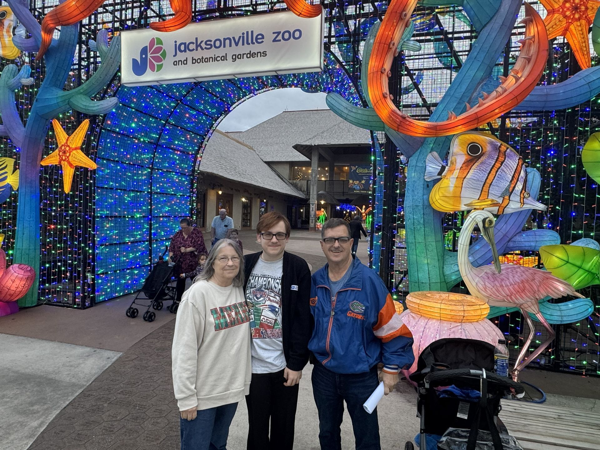 Three people posing at Jacksonville Zoo entrance under bright blue holiday lights and sea-themed decorations