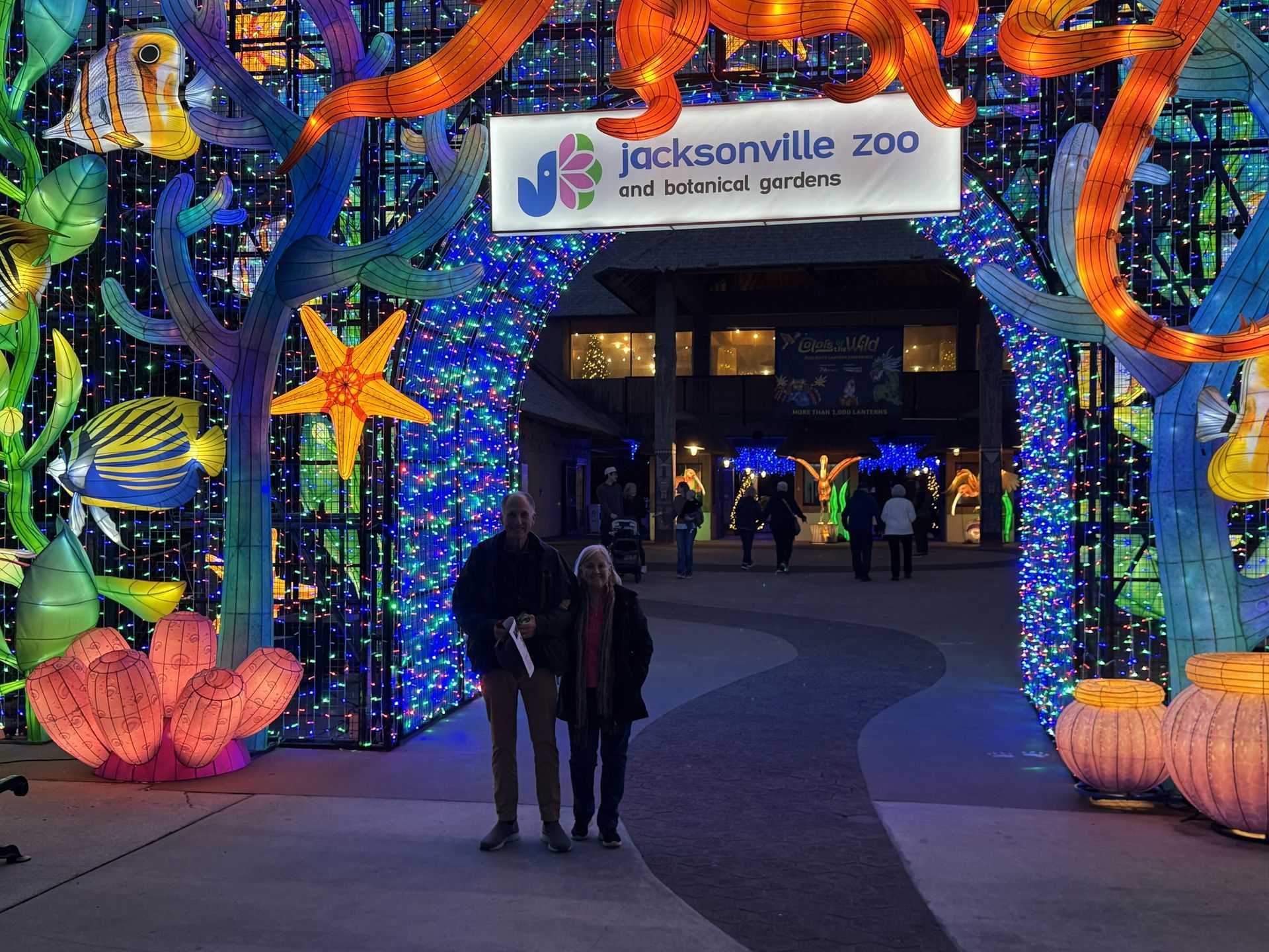Jacksonville Zoo entrance lit with colorful holiday lights, pumpkins, and two people standing under an archway