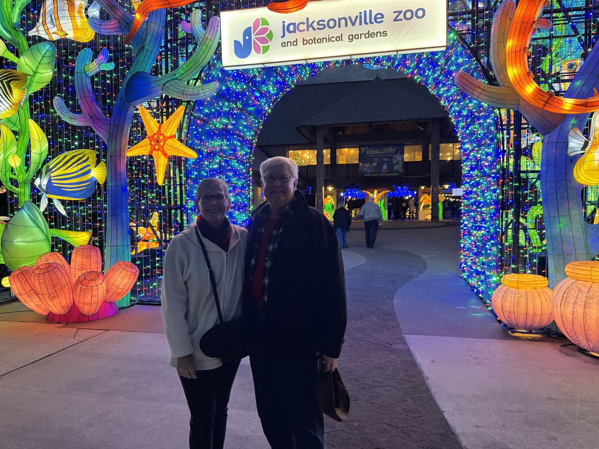 Two people silhouetted under a colorful holiday light arch at Jacksonville Zoo entrance