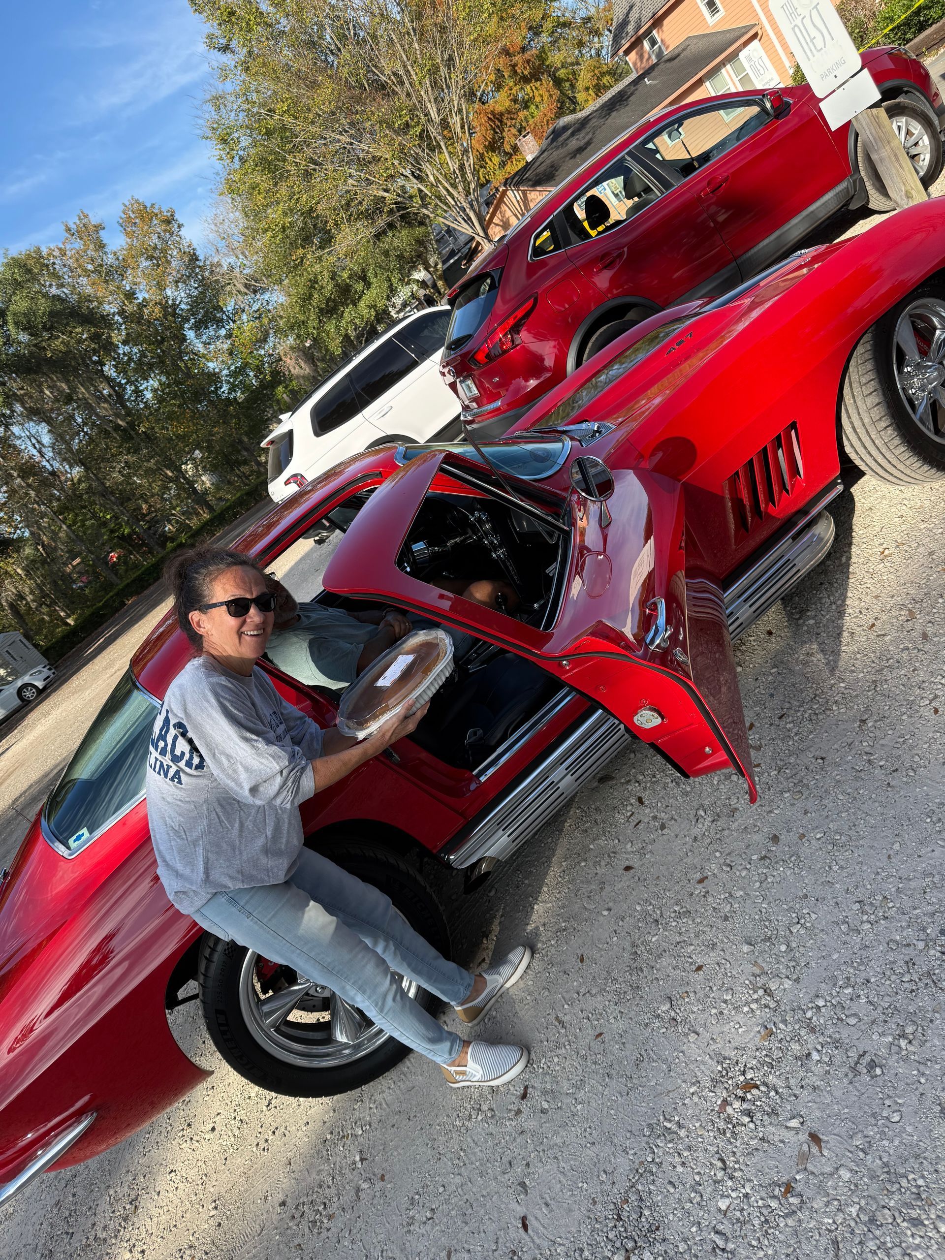 Person crouches beside a red sports car with its hood open in a driveway.