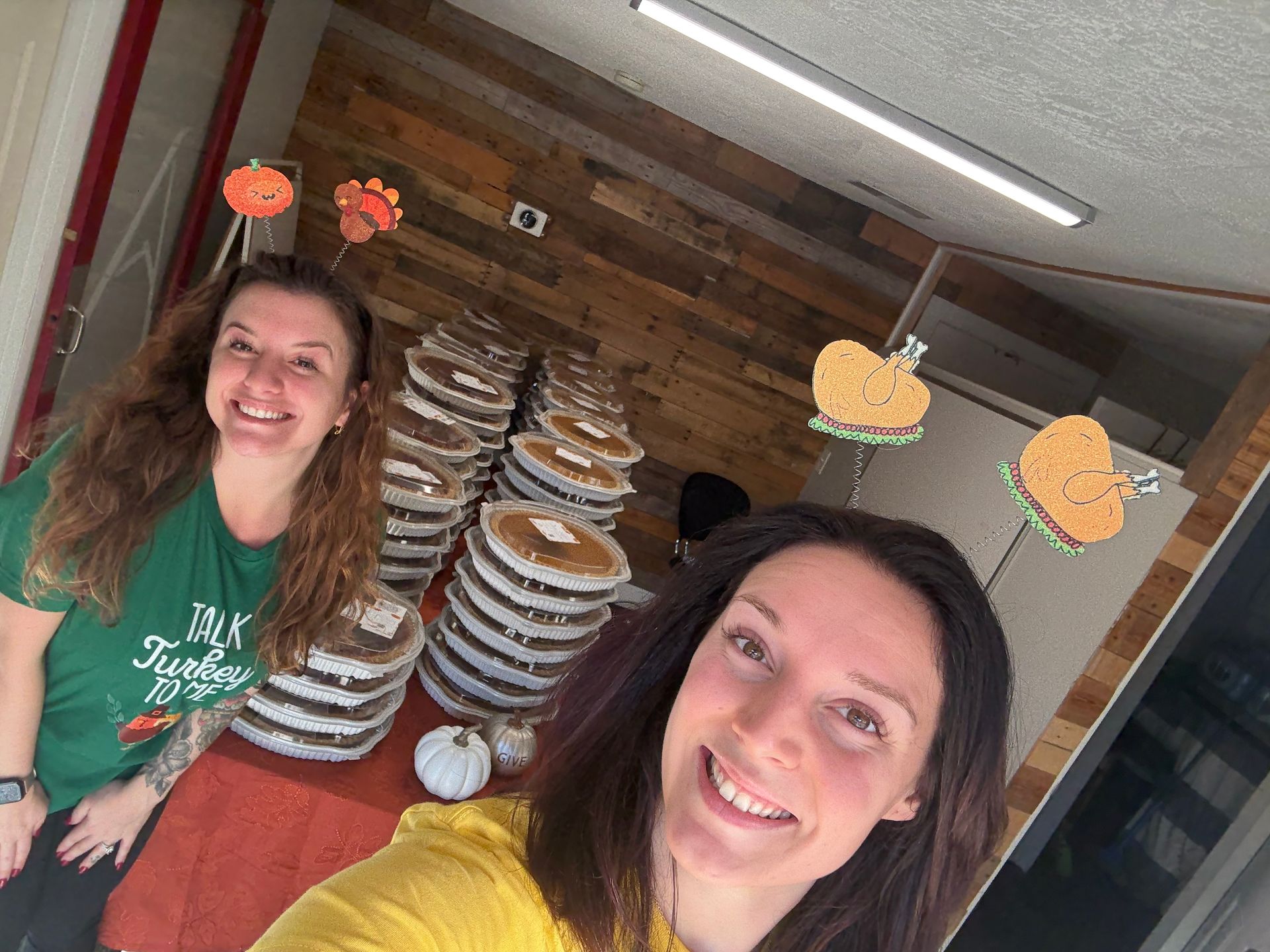 Two smiling people in a bakery, posing beside stacks of pastries on trays, with playful cartoon stickers above them.