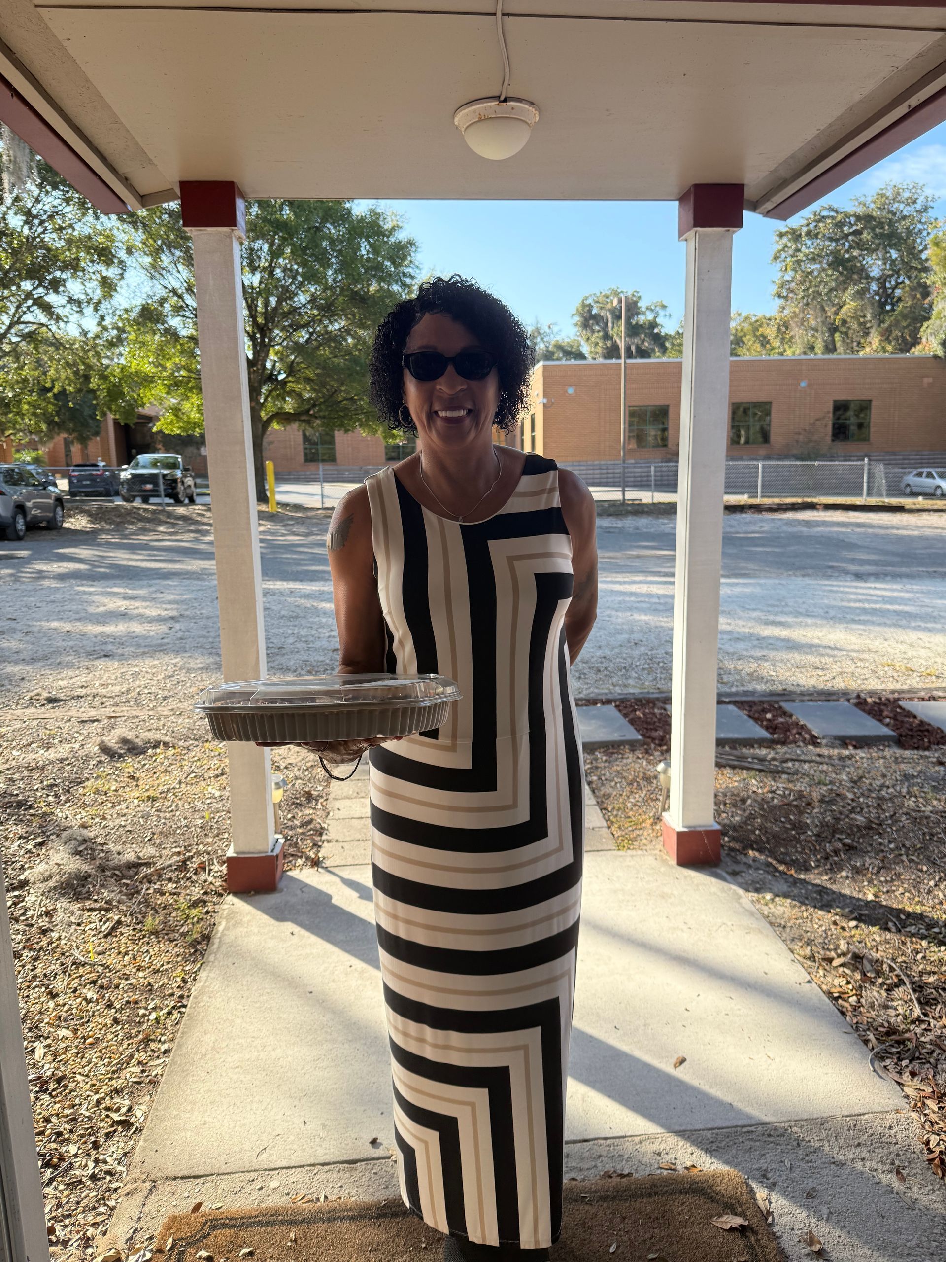 Woman in black-and-white striped dress standing on a sunlit walkway under a covered patio.