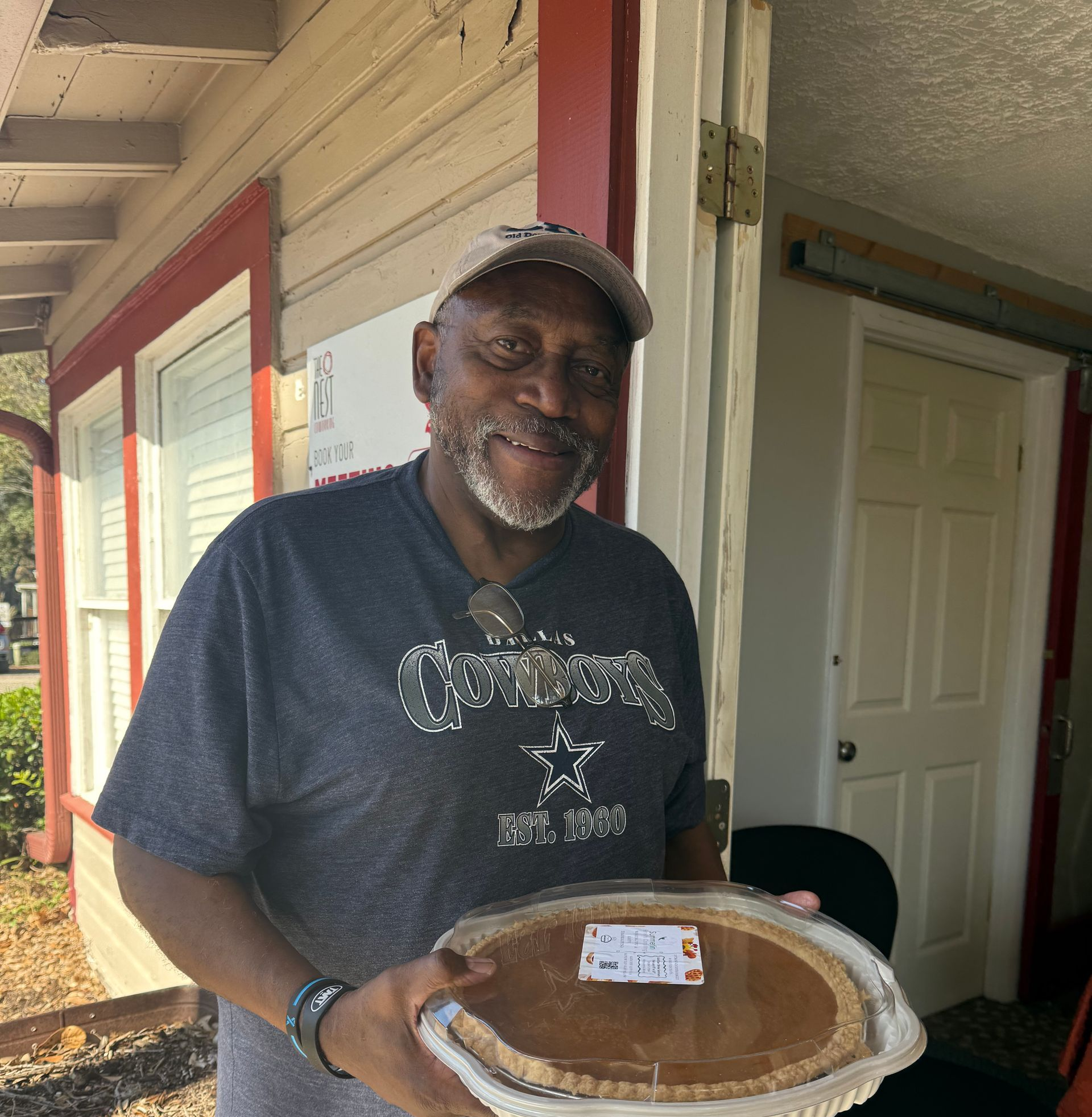 Man holding a pie on a porch, smiling beside an open doorway