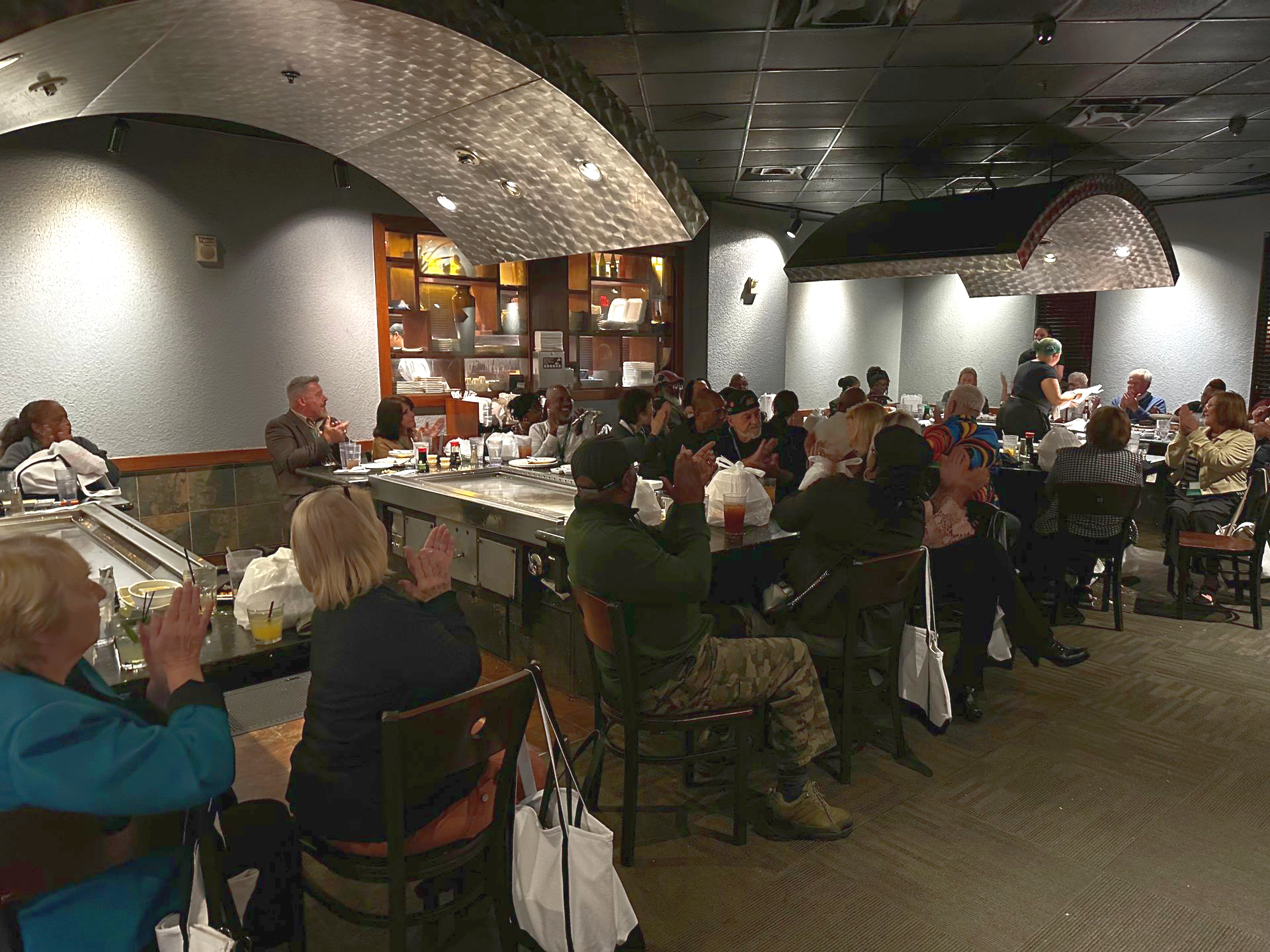 Crowded restaurant with diners seated at tables under curved metal ceilings and warm lighting