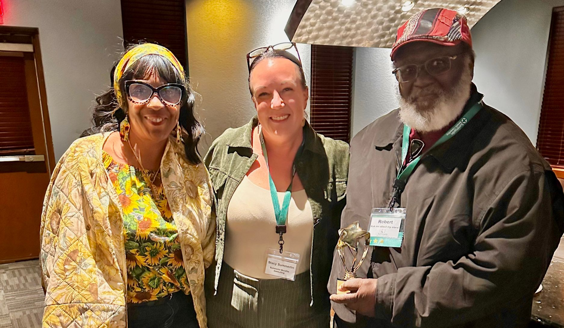 Three smiling people posing indoors at a conference, wearing lanyards and badges.