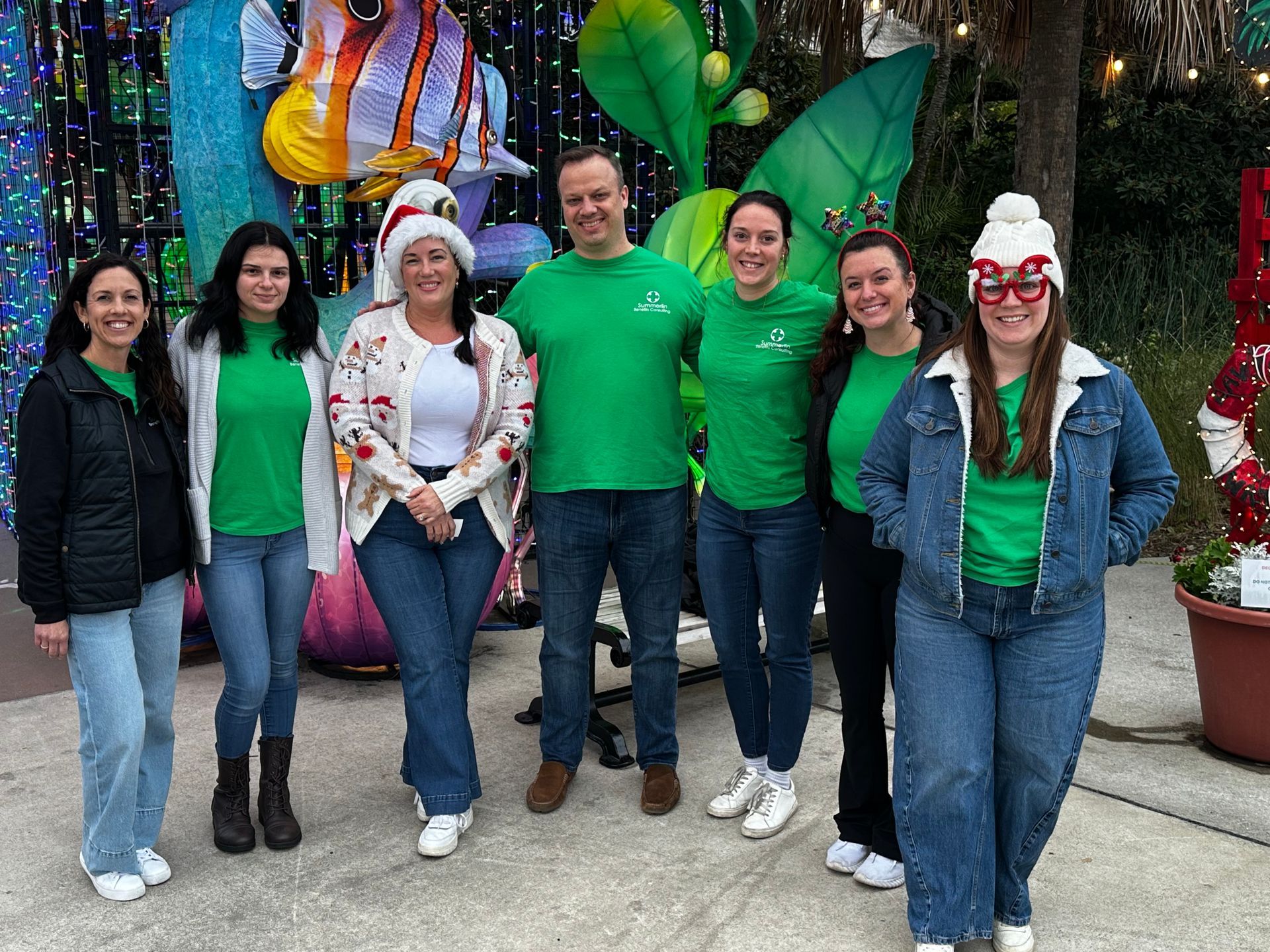 Group of people in green shirts and Santa hats posing in front of colorful holiday decorations