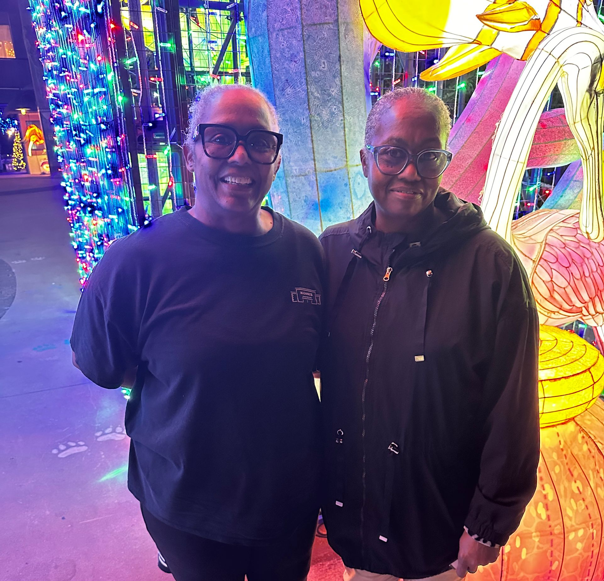 Two people standing together in a colorful, neon-lit art installation, smiling at the camera.