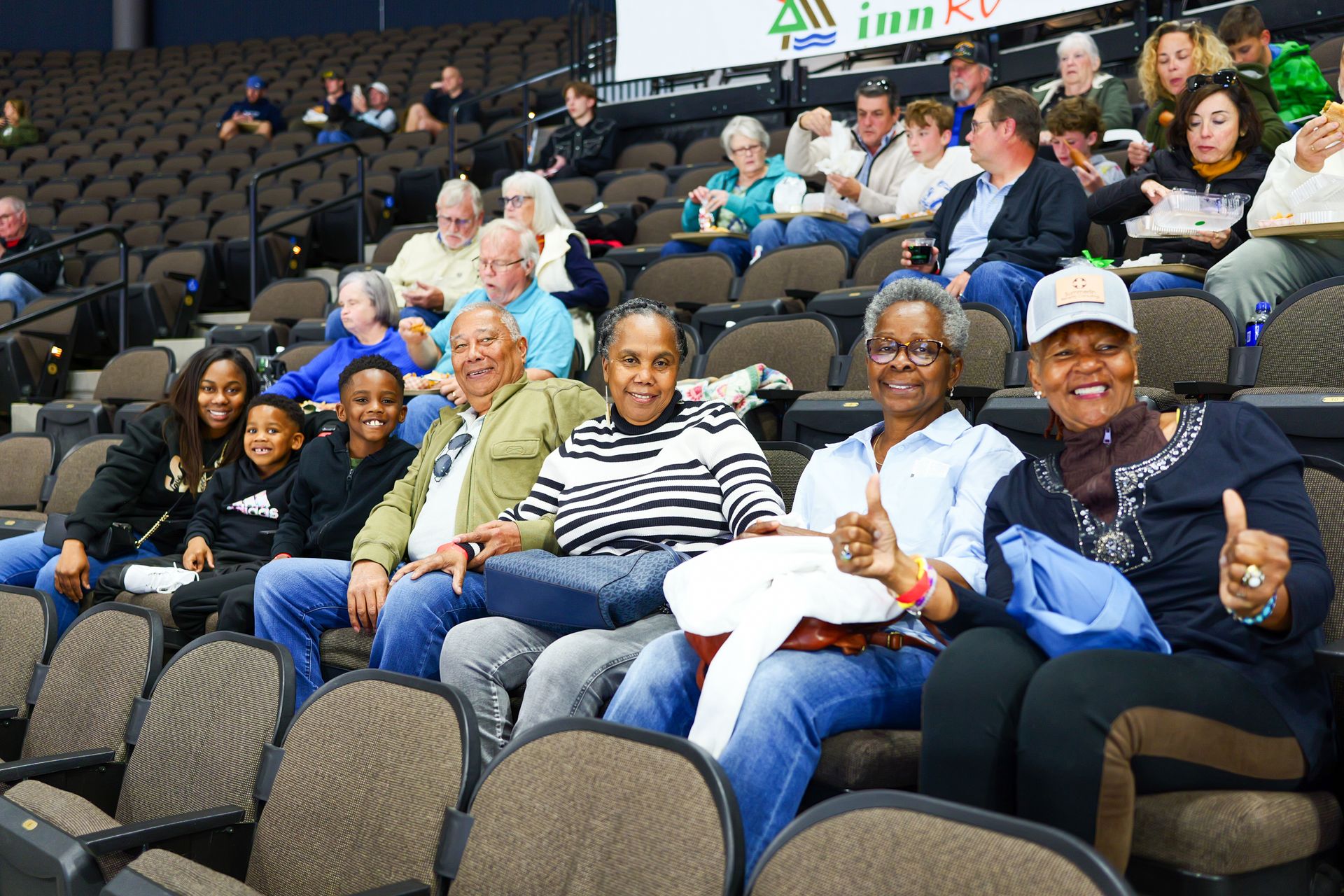 A group of people are sitting in a stadium giving a thumbs up