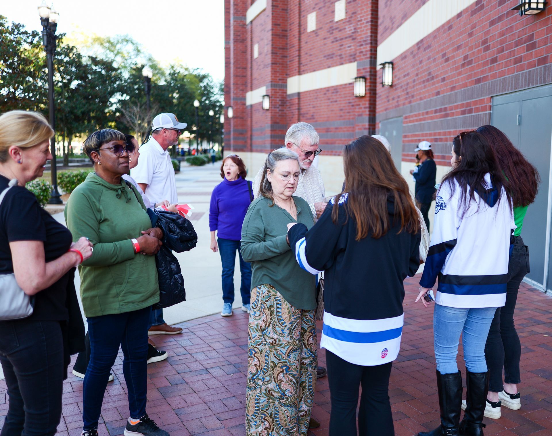 A group of people are standing on a brick sidewalk talking to each other.