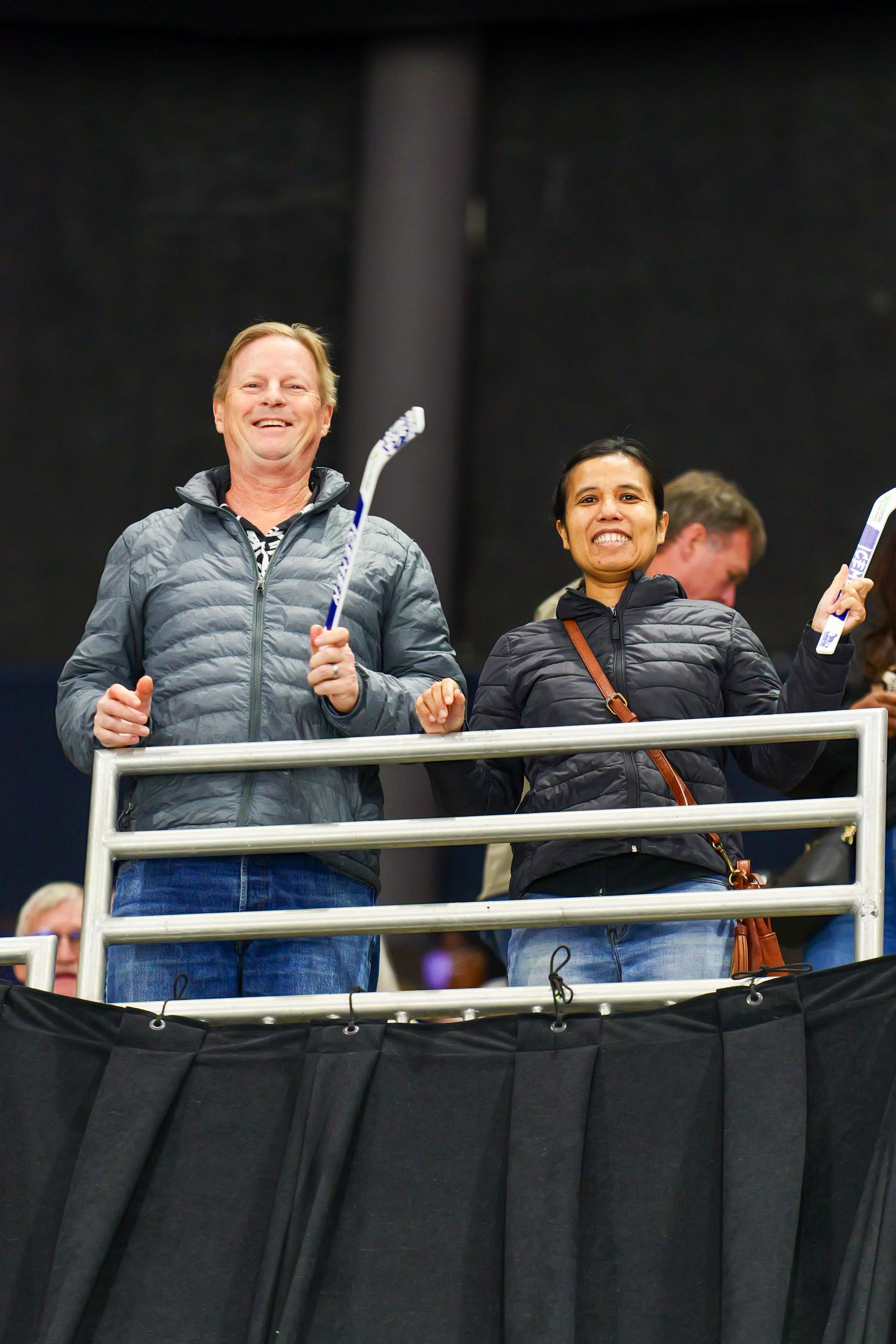 A man and a woman are standing behind a fence holding hockey sticks.