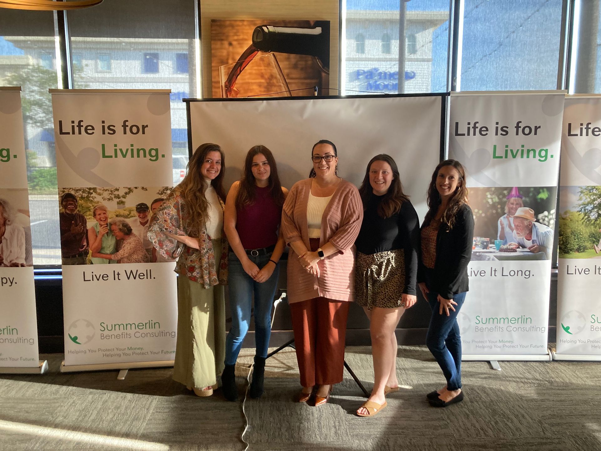 A group of women standing next to each other in front of a sign that says `` life is for living ''.