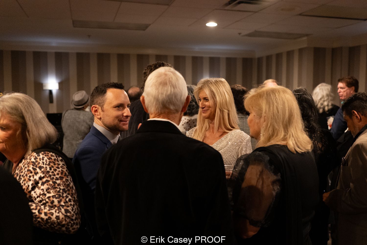 A group of people are standing in a room talking to each other.