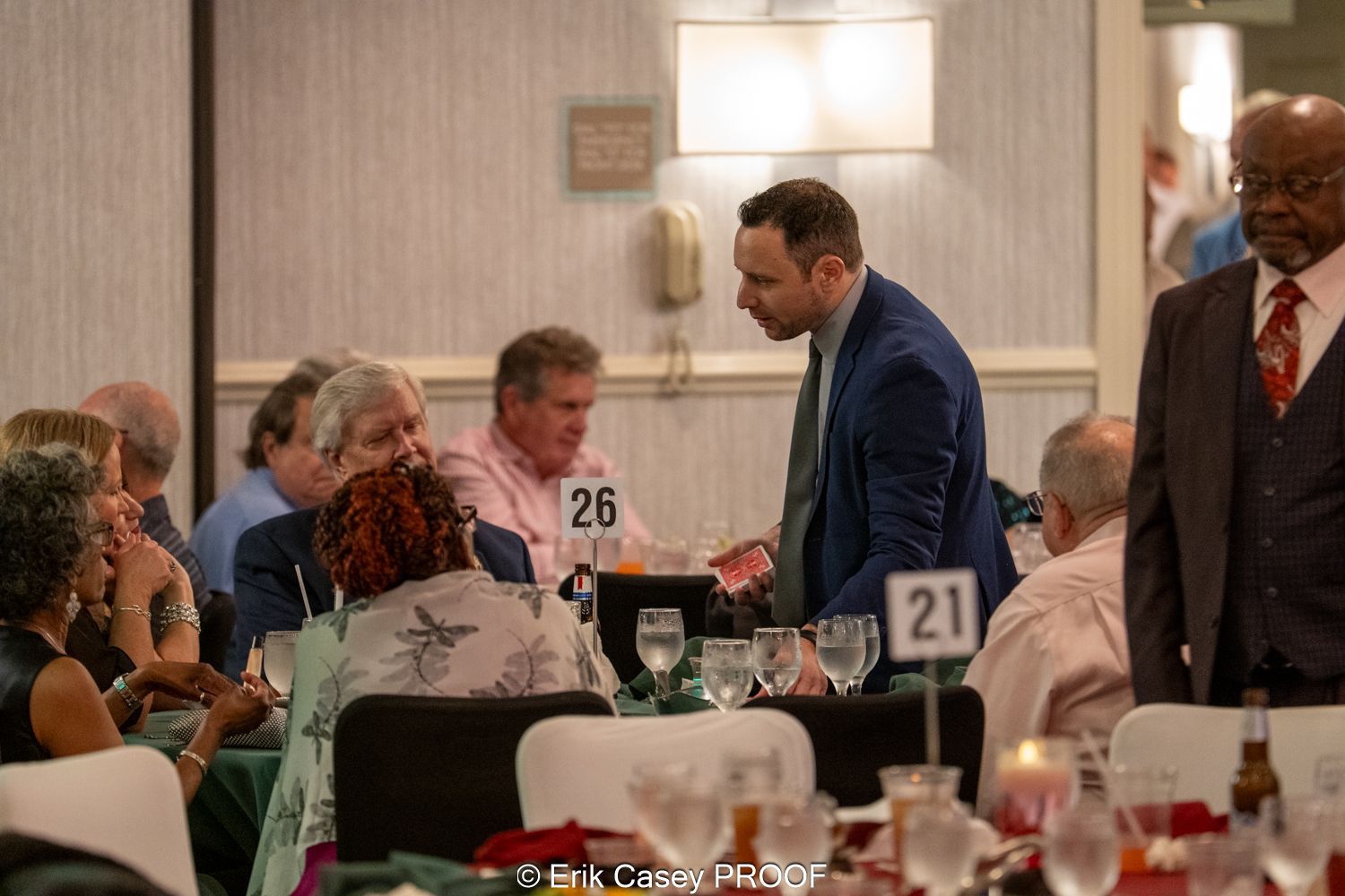 A man in a suit is standing in front of a table with a number 21 on it.