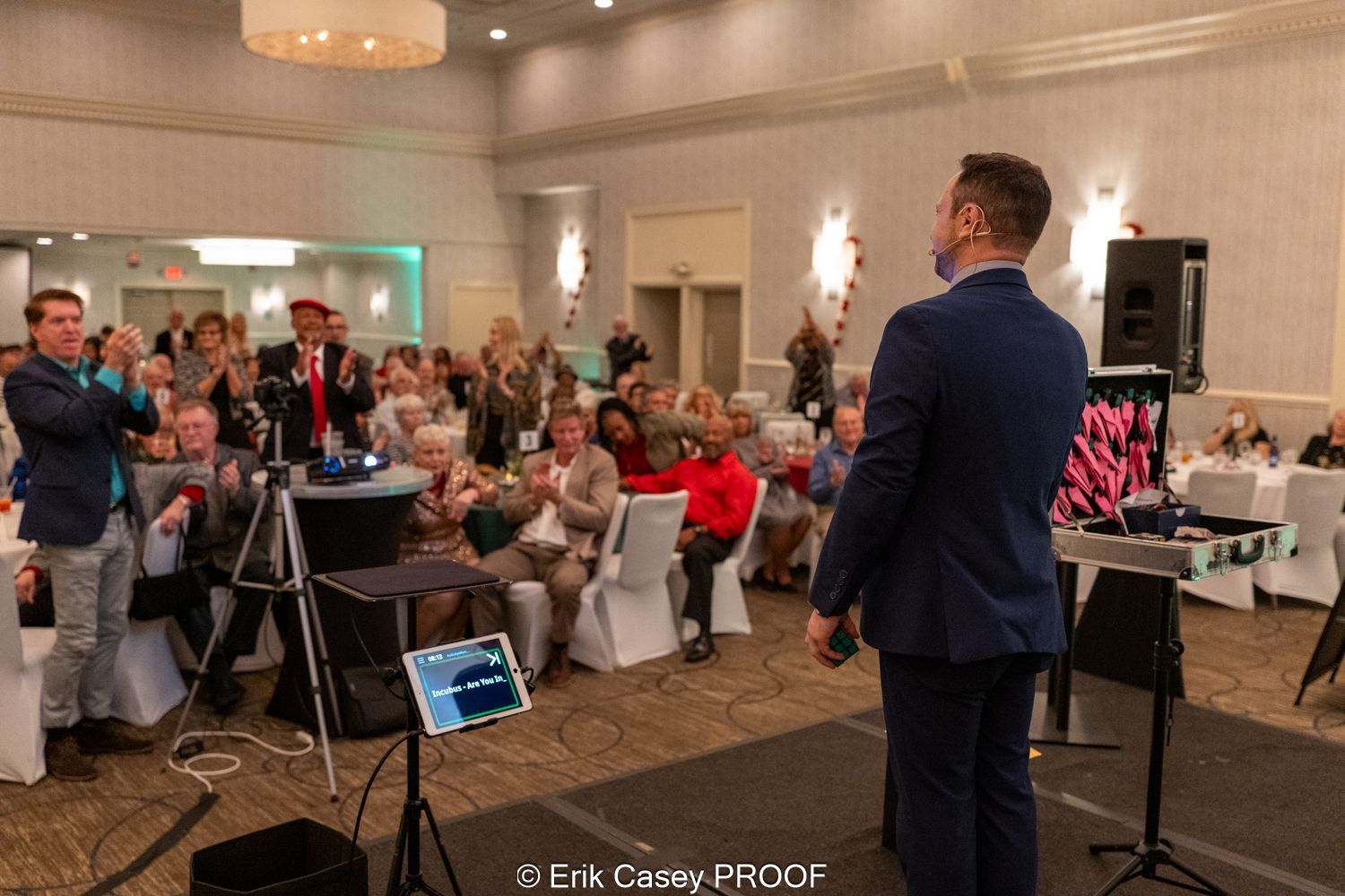 A man in a suit is standing in front of a crowd of people in a room.