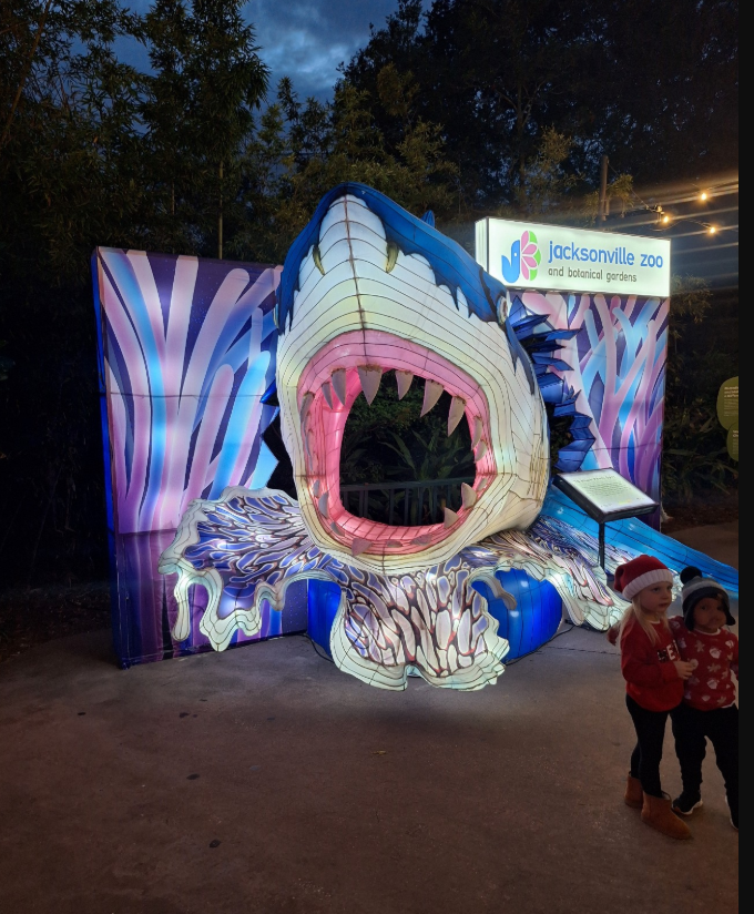 Illuminated dinosaur mouth exhibit at a night event, with two children standing nearby