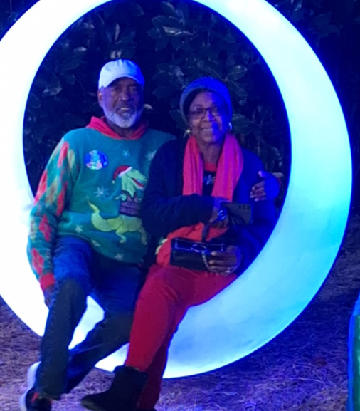 Two people sitting together on a glowing crescent-shaped light sculpture at night