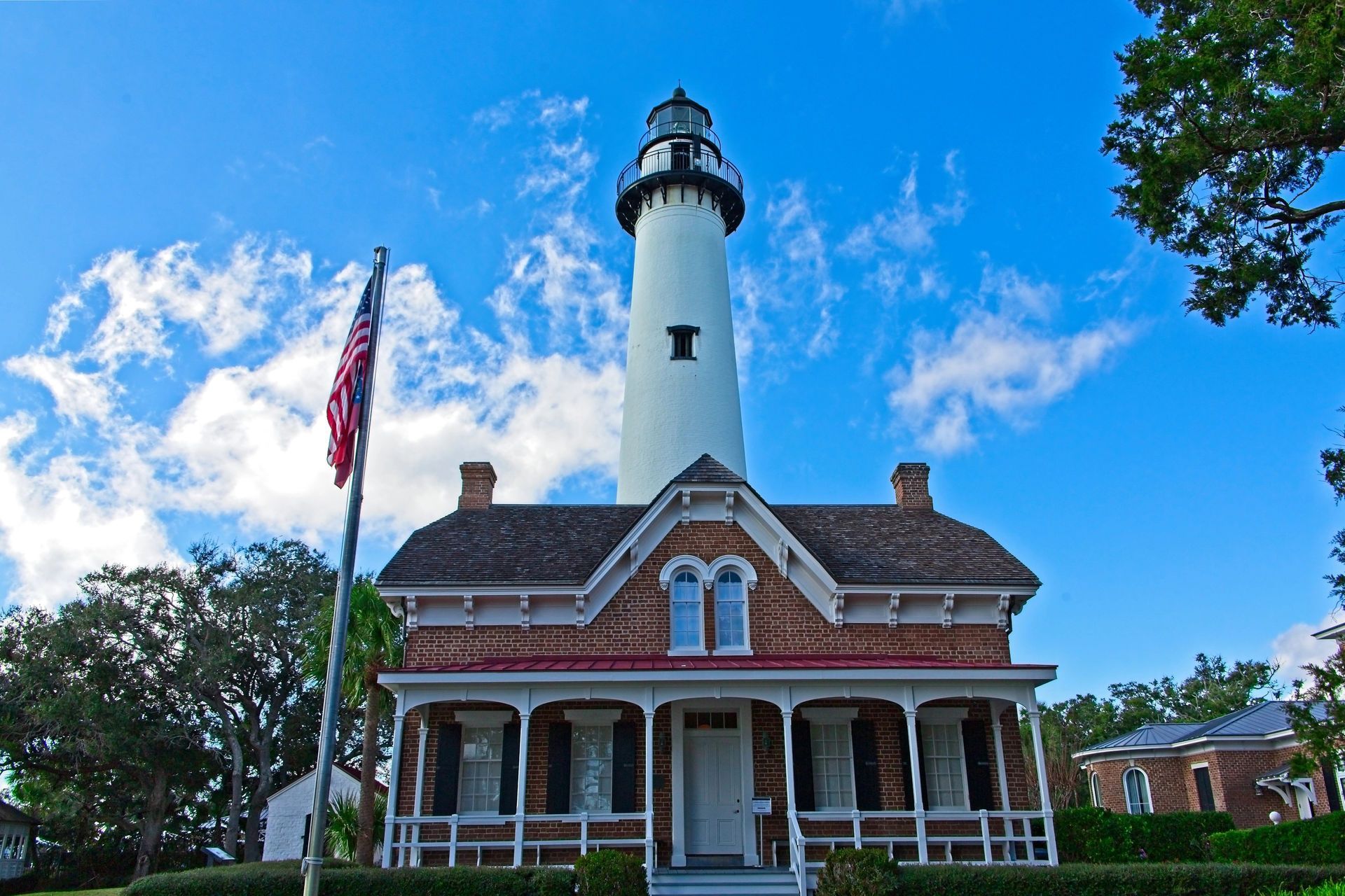Historic lighthouse with brick keeper’s house, American flag, and blue sky with clouds, St. Simons Island, GA