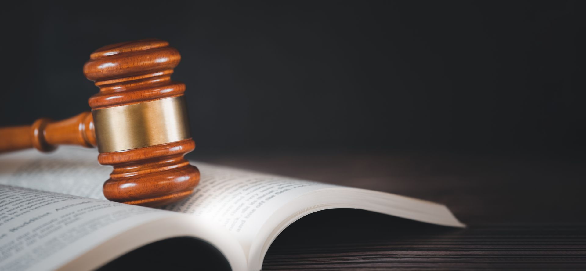 Brown and gold gavel sitting on an open book with black background.