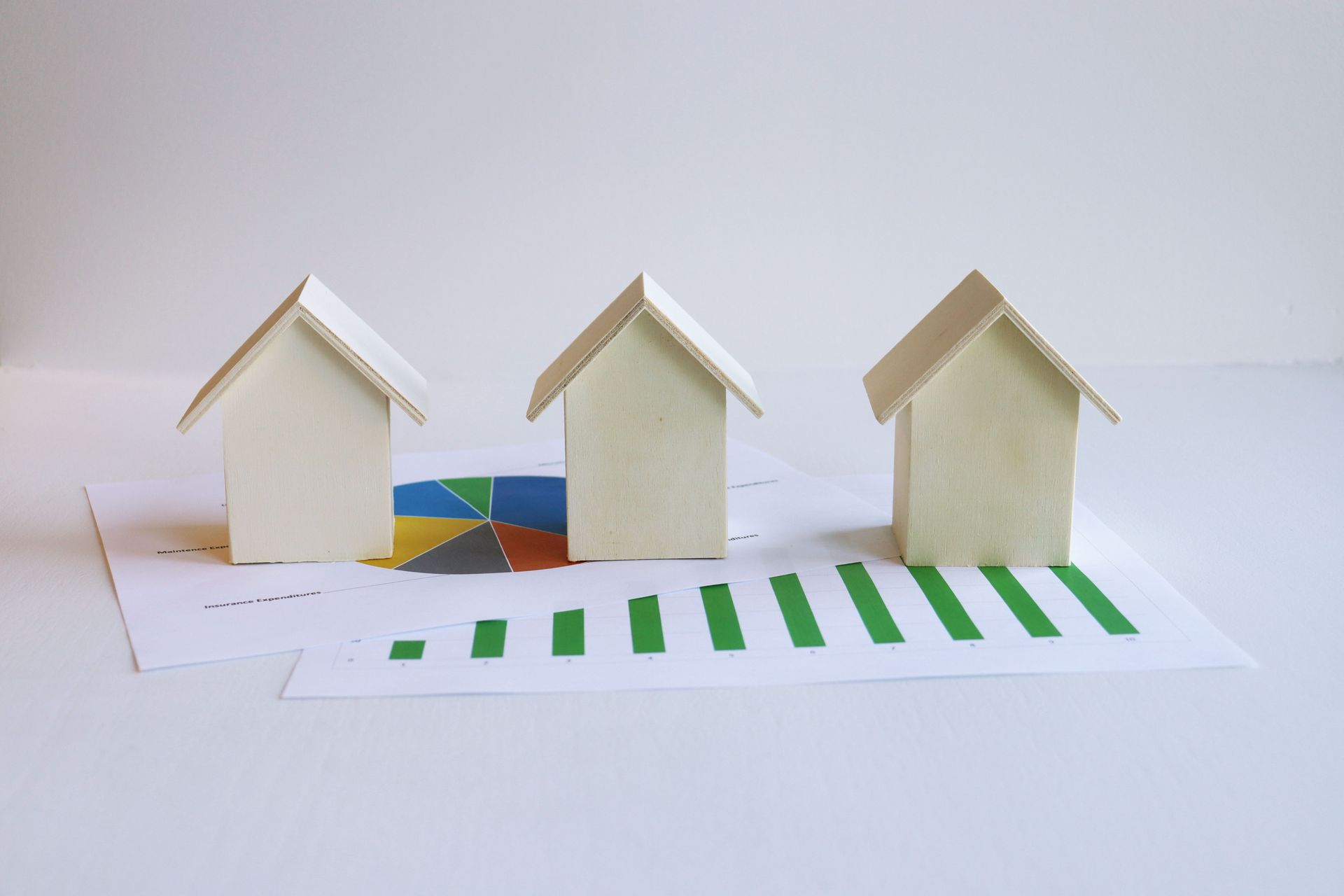 Three small cardboard houses on a white surface with a green striped path in front