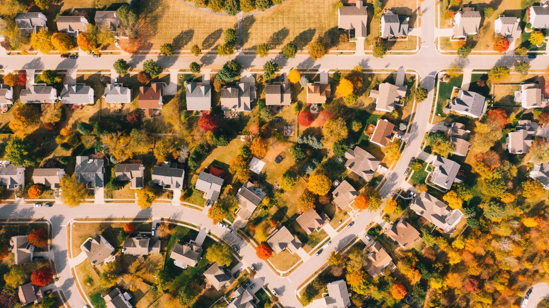 Aerial view of a suburban neighborhood with houses, streets, and autumn-colored trees.
