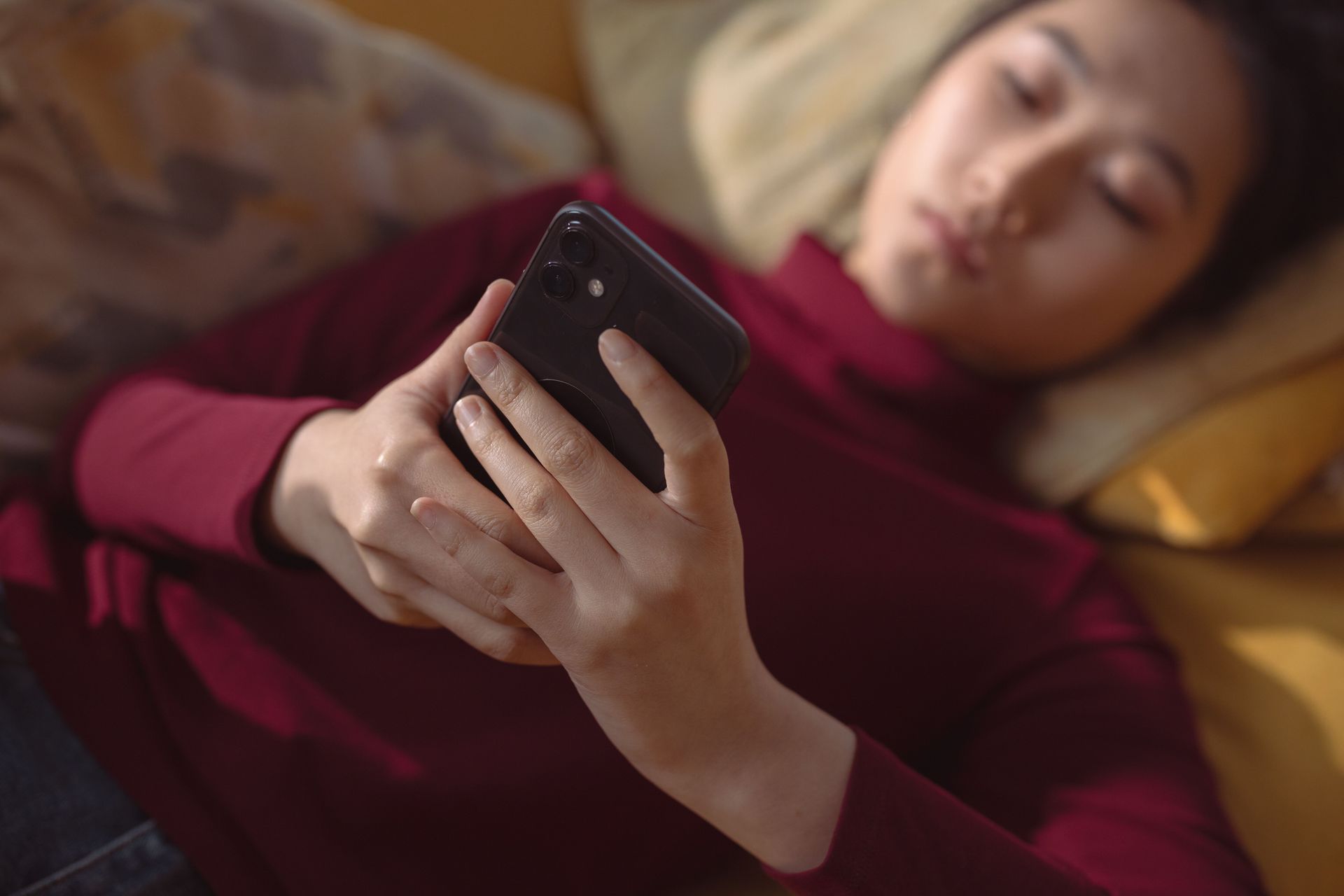 Person lying in bed, holding a smartphone and looking at the screen in a dimly lit room