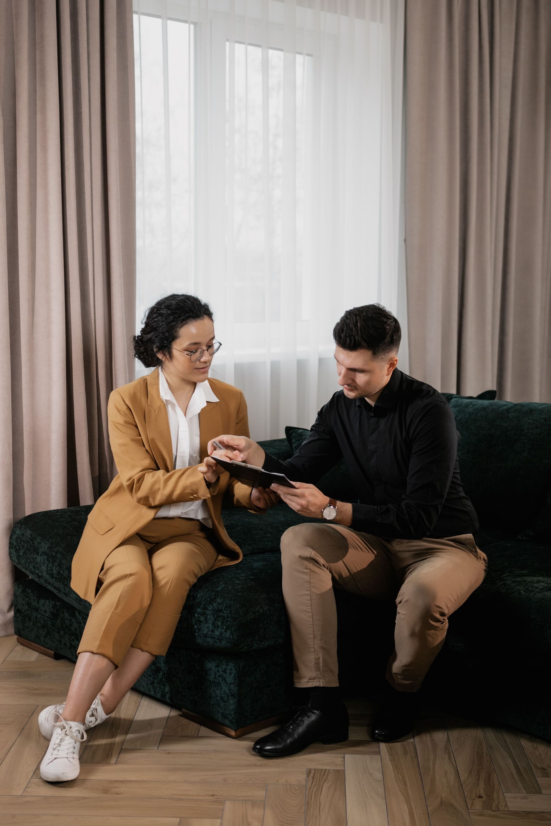 Two people sit on a sofa, looking at a phone in a bright living room.