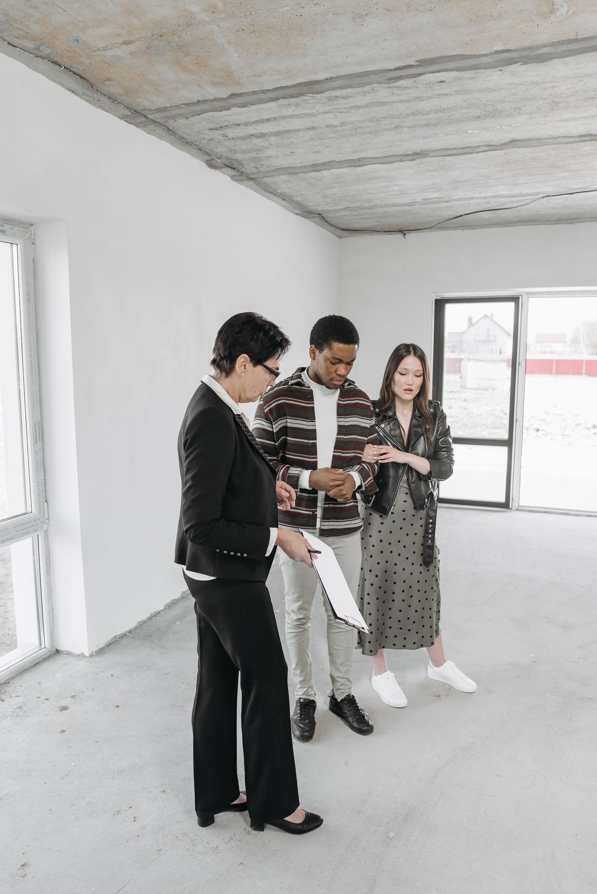 Three people standing in an unfinished room, reviewing papers near a window.