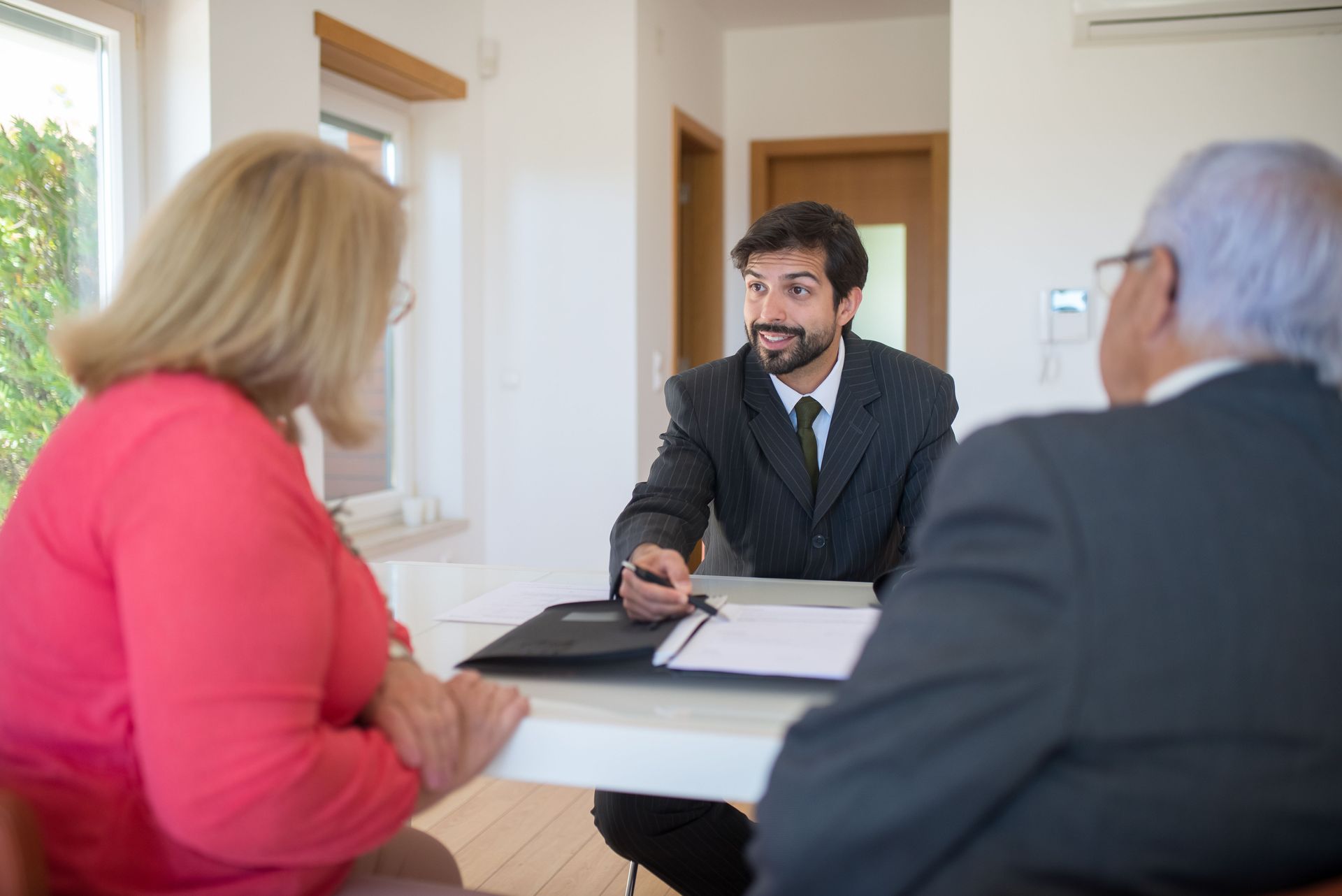 Three people in a bright office meeting, discussing documents across a desk