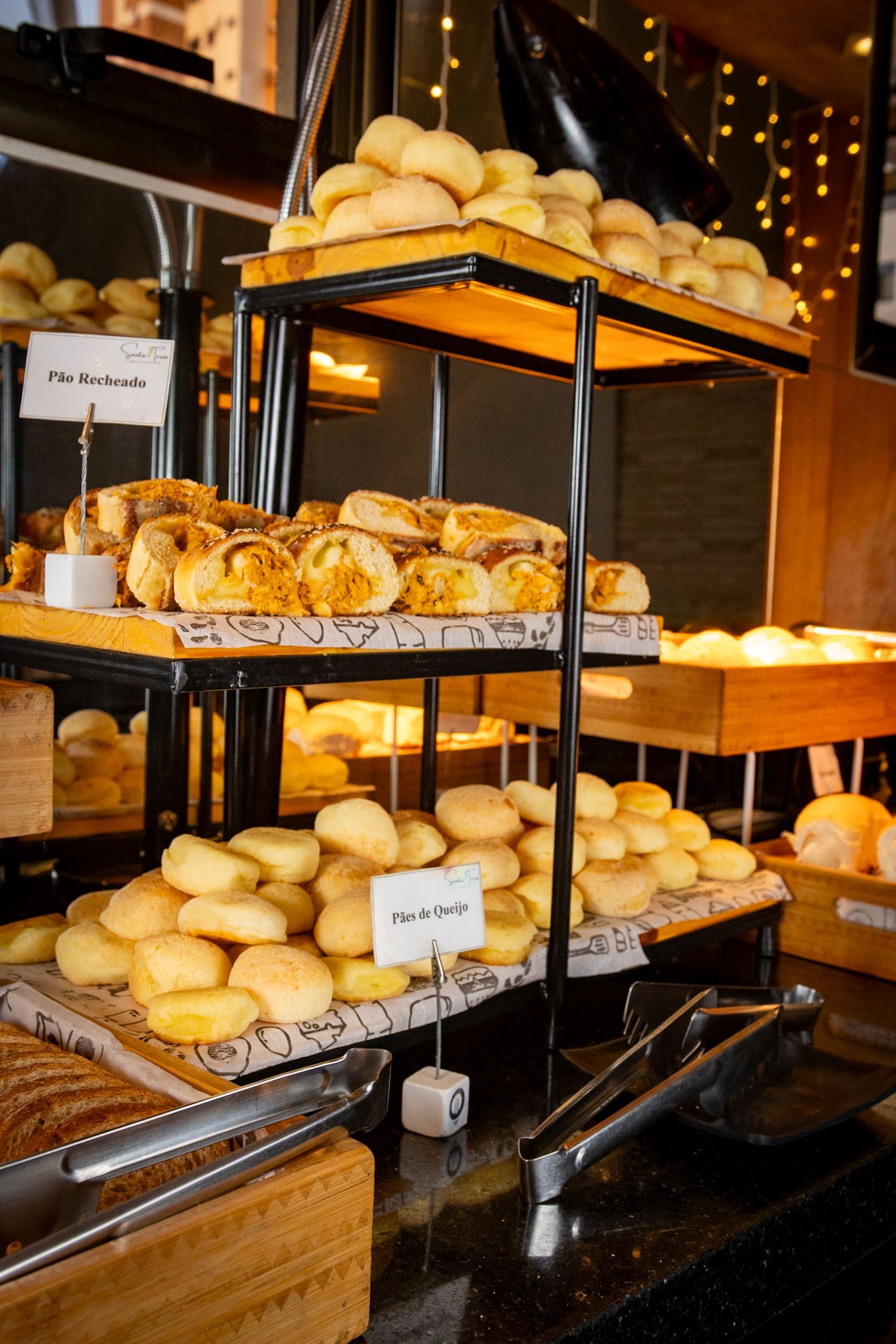 Vitrine de padaria com diversos pães e doces em prateleiras de vários níveis.