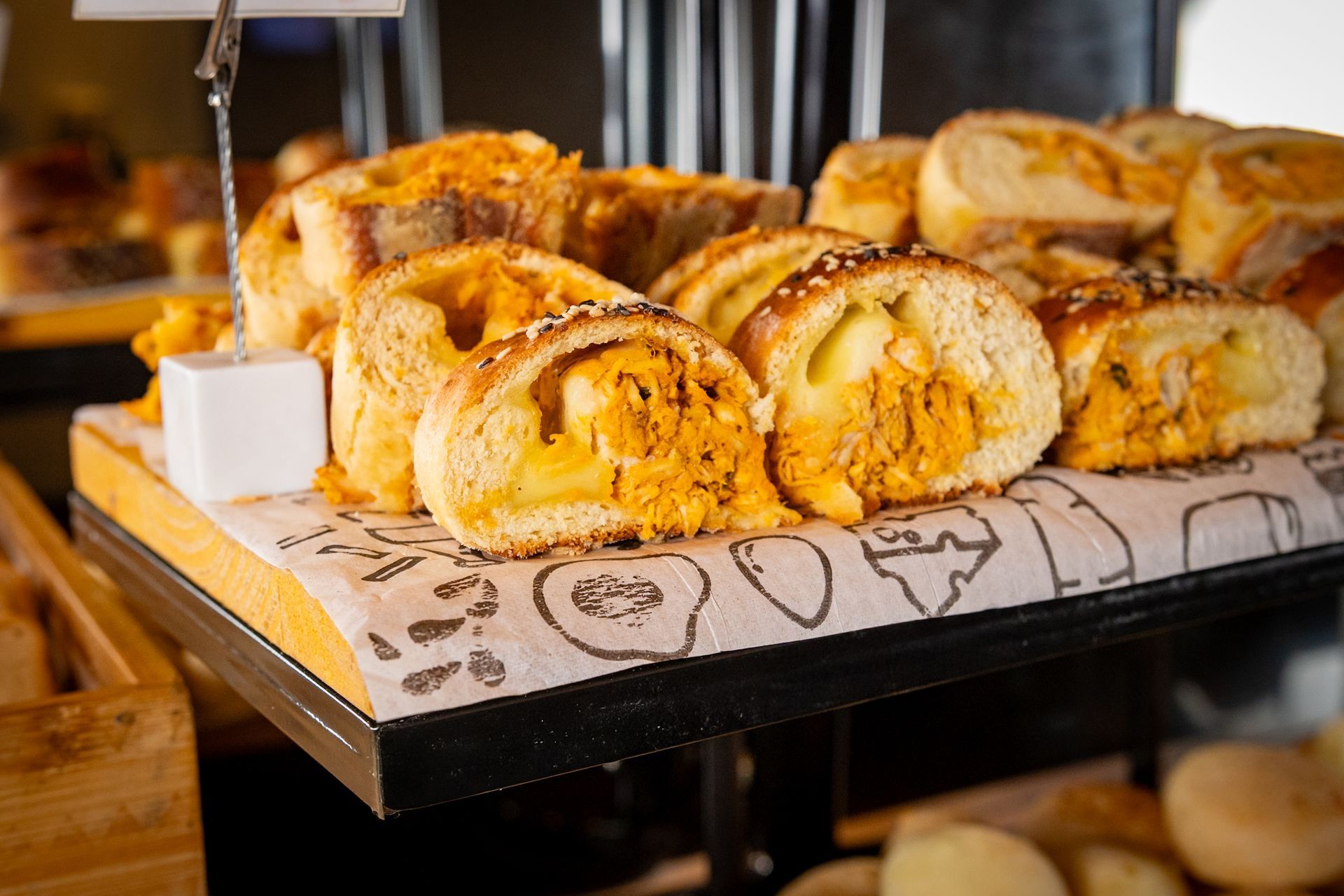 Pãezinhos fatiados recheados com carne desfiada, expostos junto com outros pães.