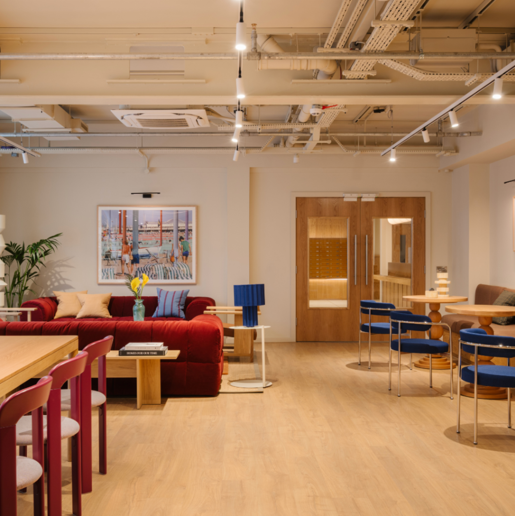 Bright, modern lounge with red sofas, blue chairs, wooden tables, and artwork on the wall