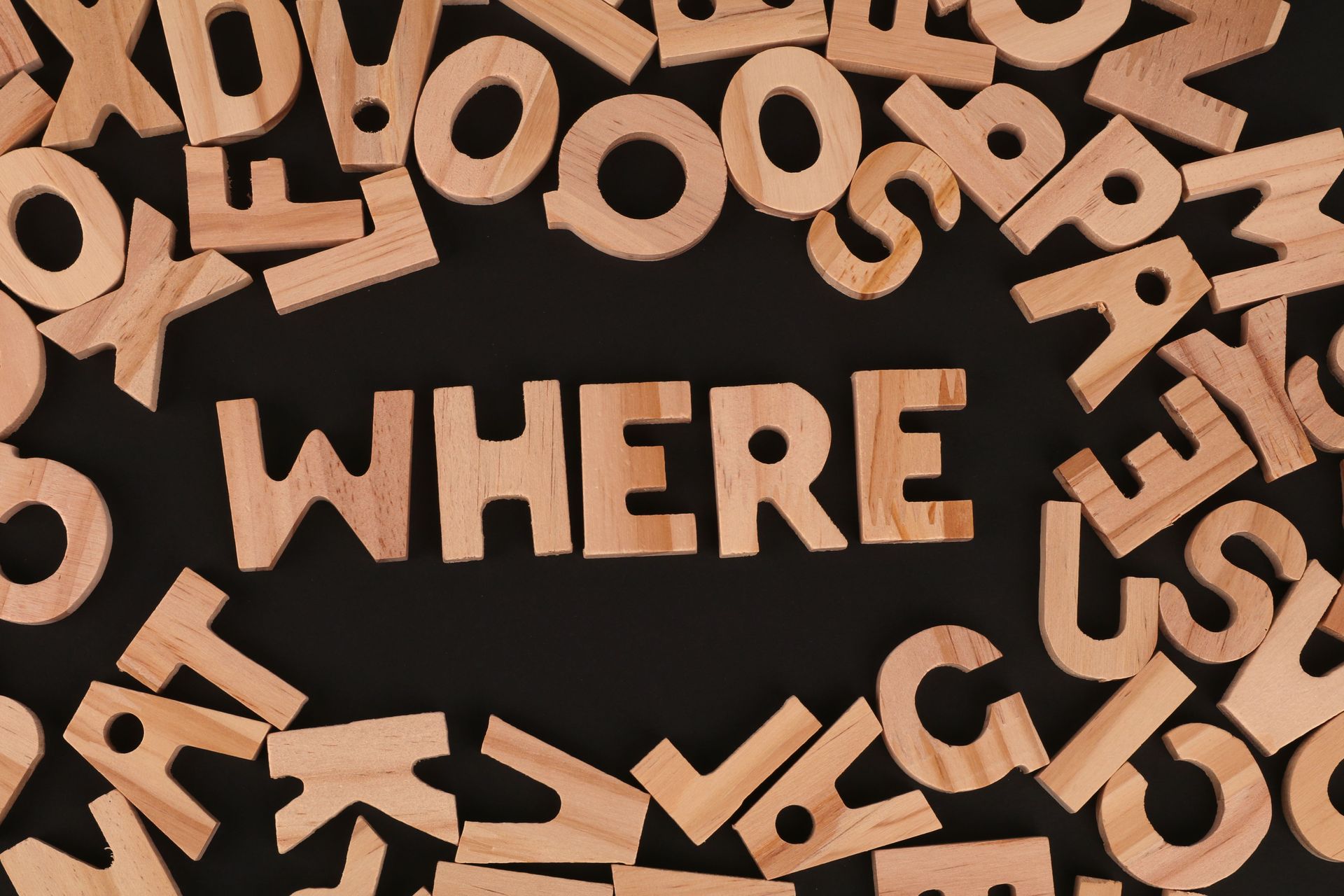 Wooden letters scattered around the word “WHERE” on a dark background.