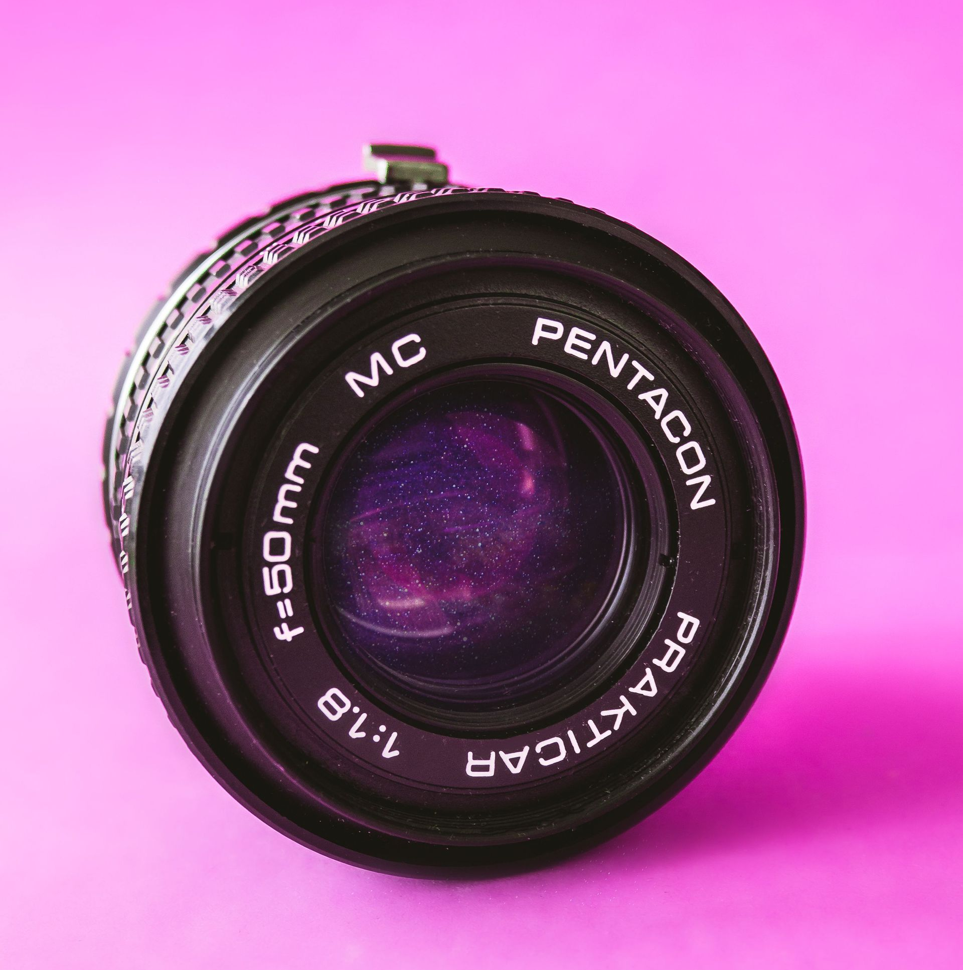 Close-up of a black MC Pentacon Prakticar camera lens on a pink background