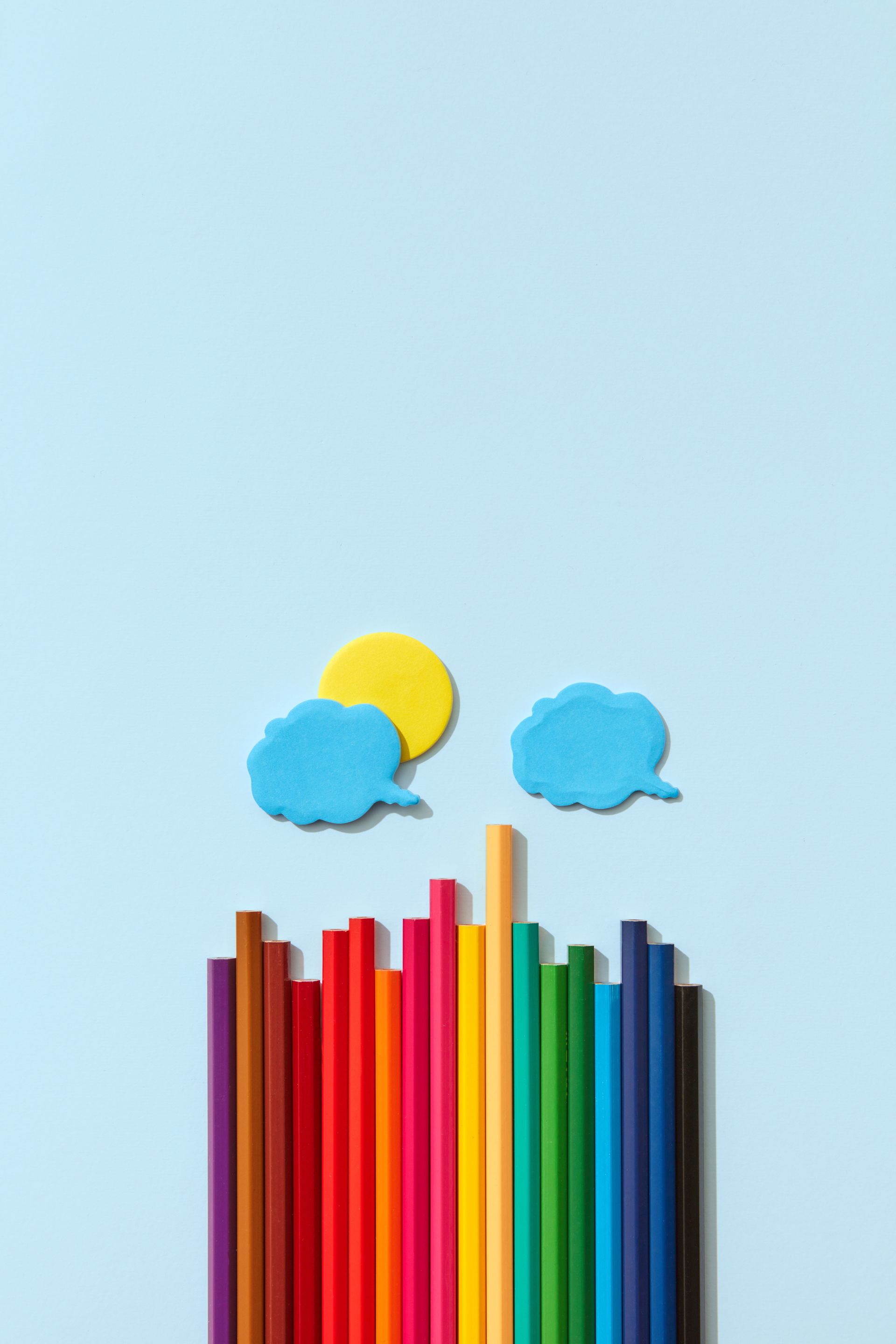 Colorful pencils with blue and yellow cloud shapes against a light blue background