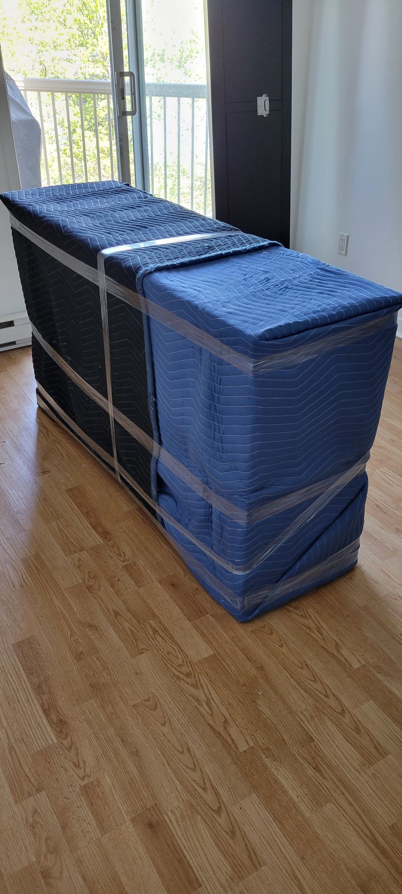 A blue box wrapped in plastic is sitting on a wooden floor in a living room.