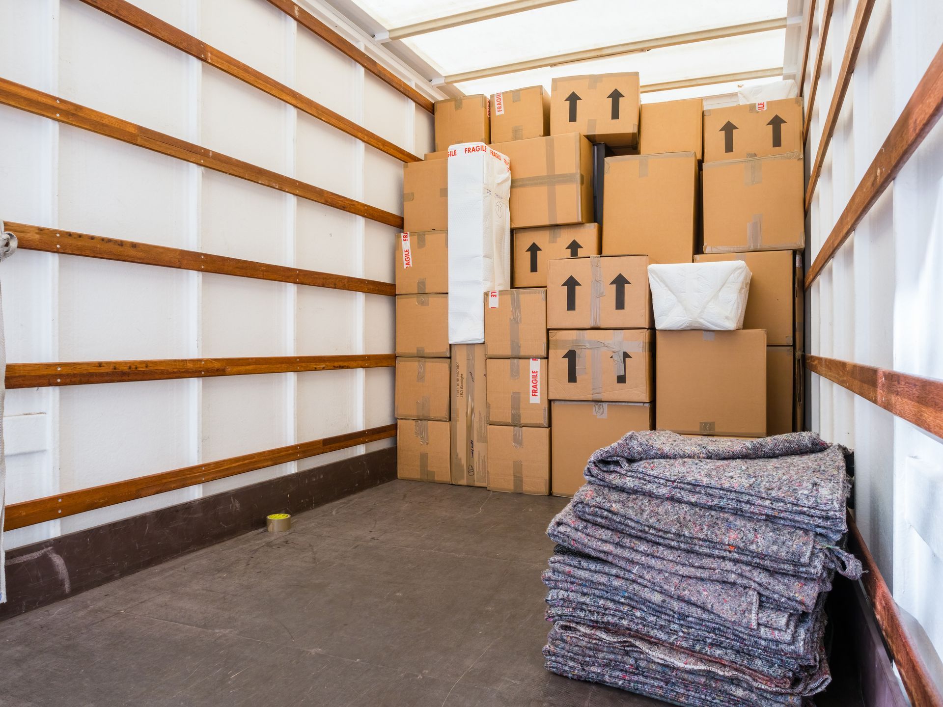 Inside a moving truck, stacked boxes and packing blankets.