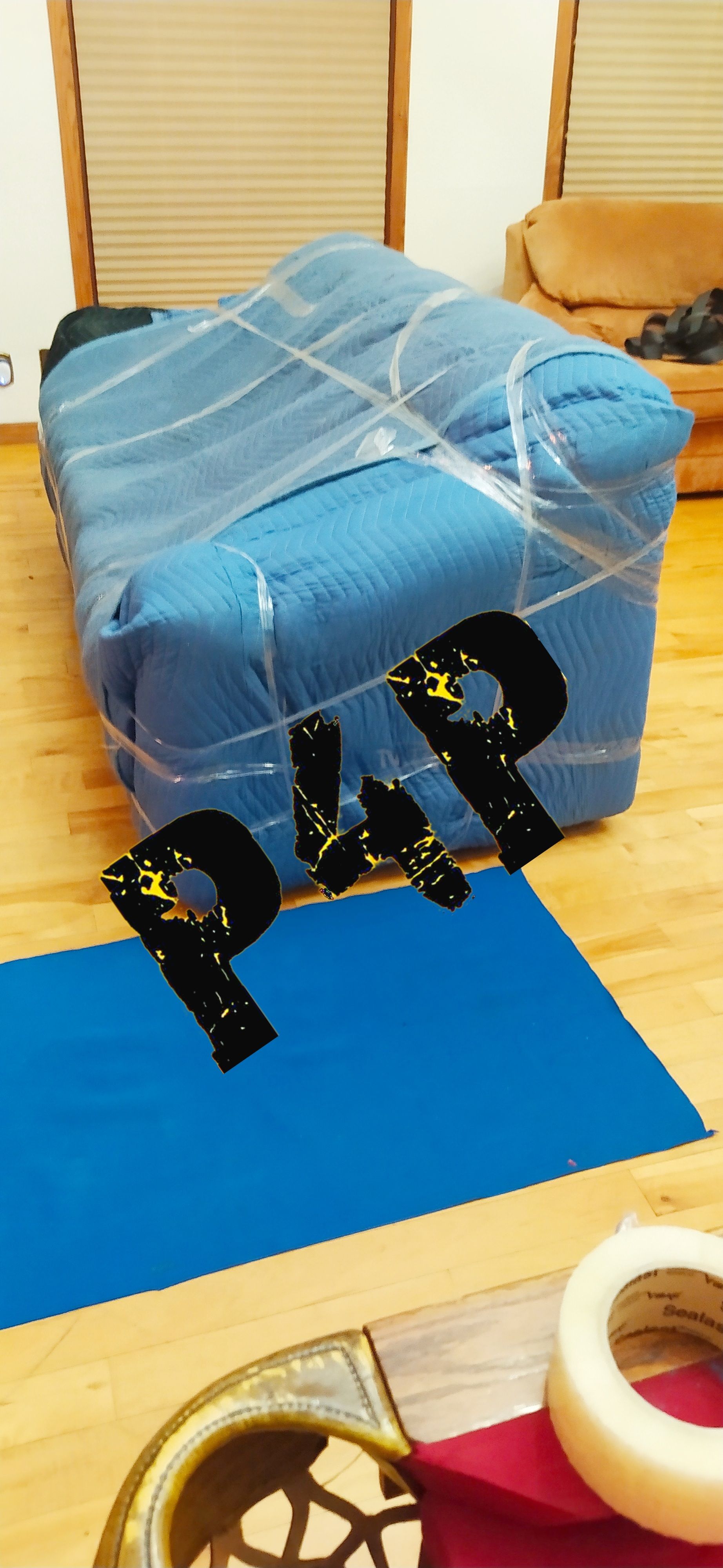 A blue couch is wrapped in plastic wrap in a living room.