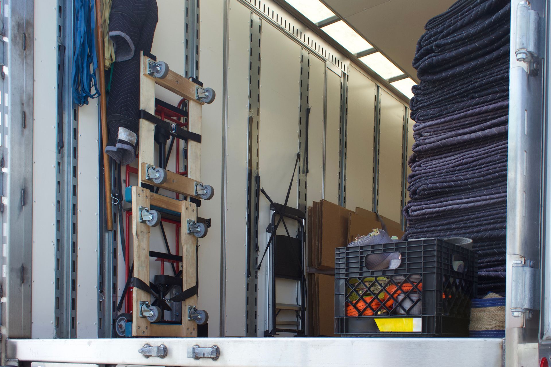 Inside of a truck, with moving supplies. A dolly, crates, boxes, and folded chairs are visible.