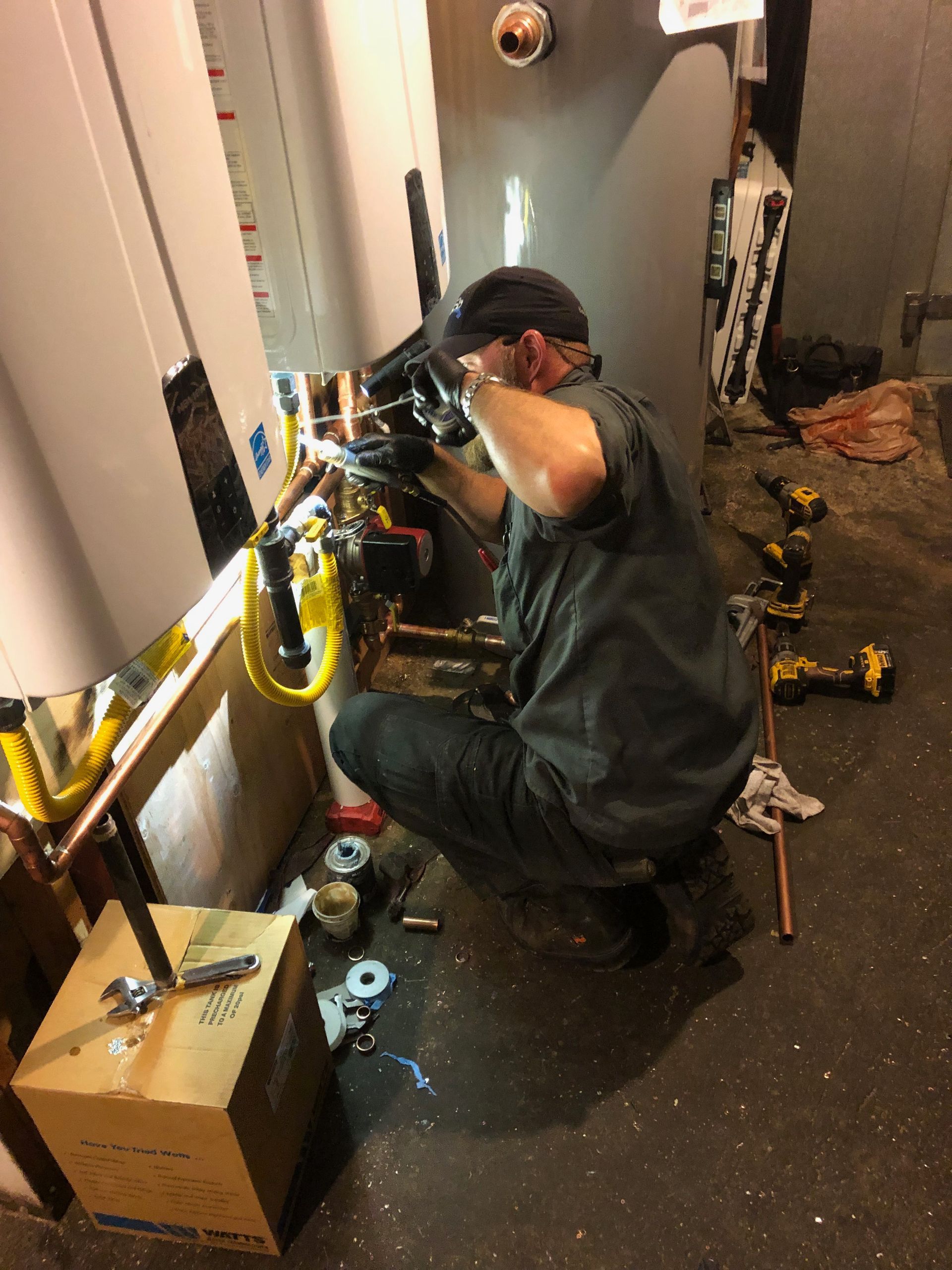 A man is working on a water heater in a basement.