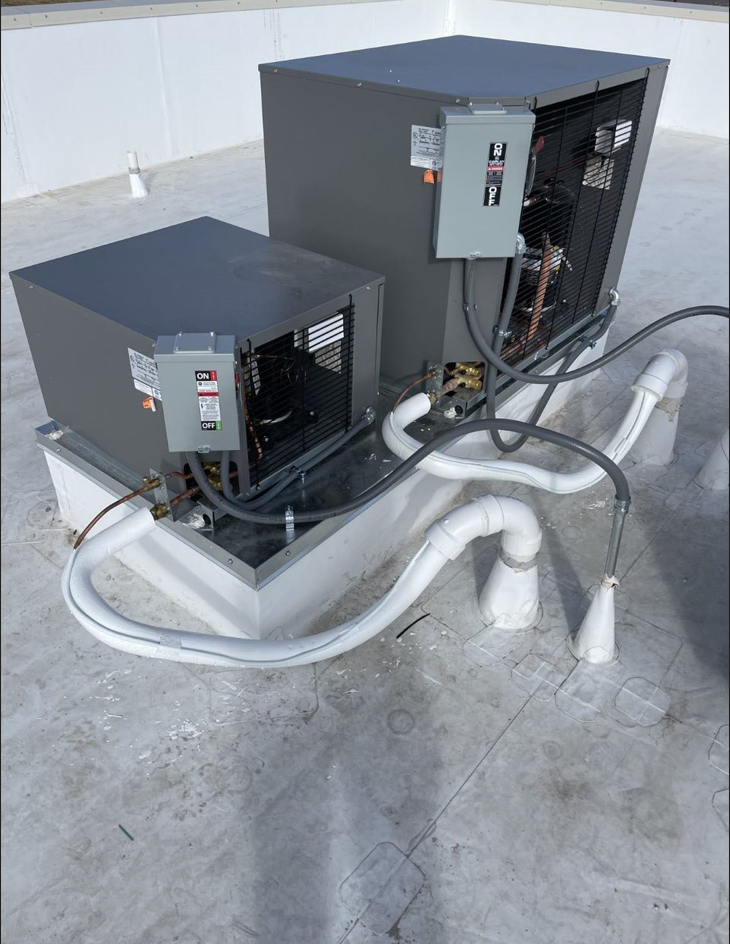 Two air conditioners are sitting on top of a concrete roof.