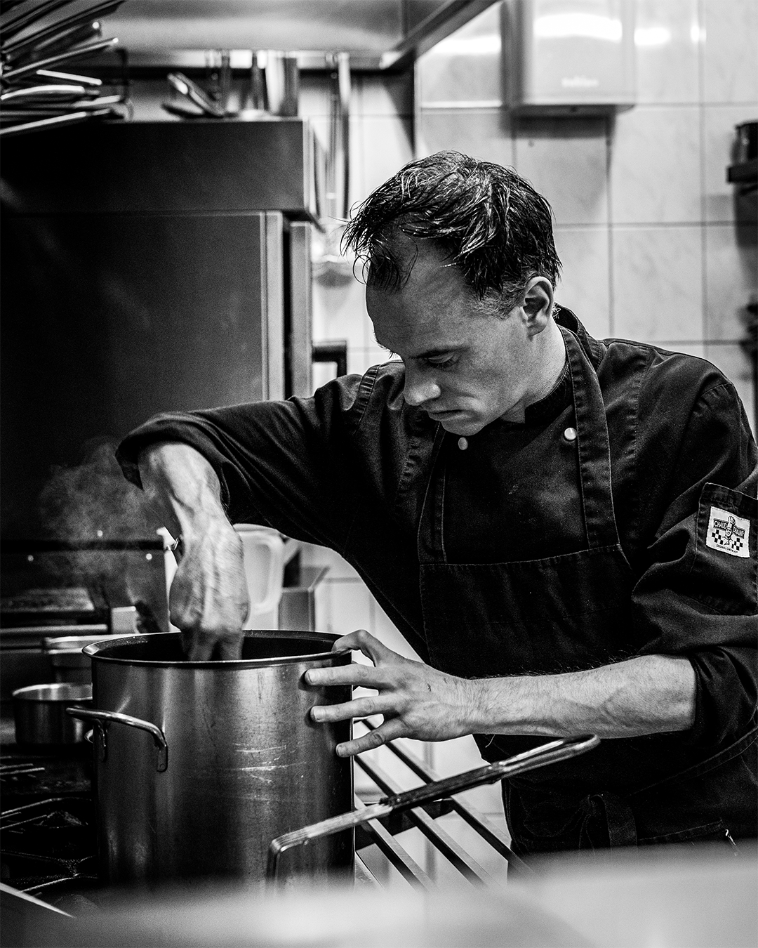 Een chef-kok roert in een pan in een professionele keuken; er stijgt stoom op.