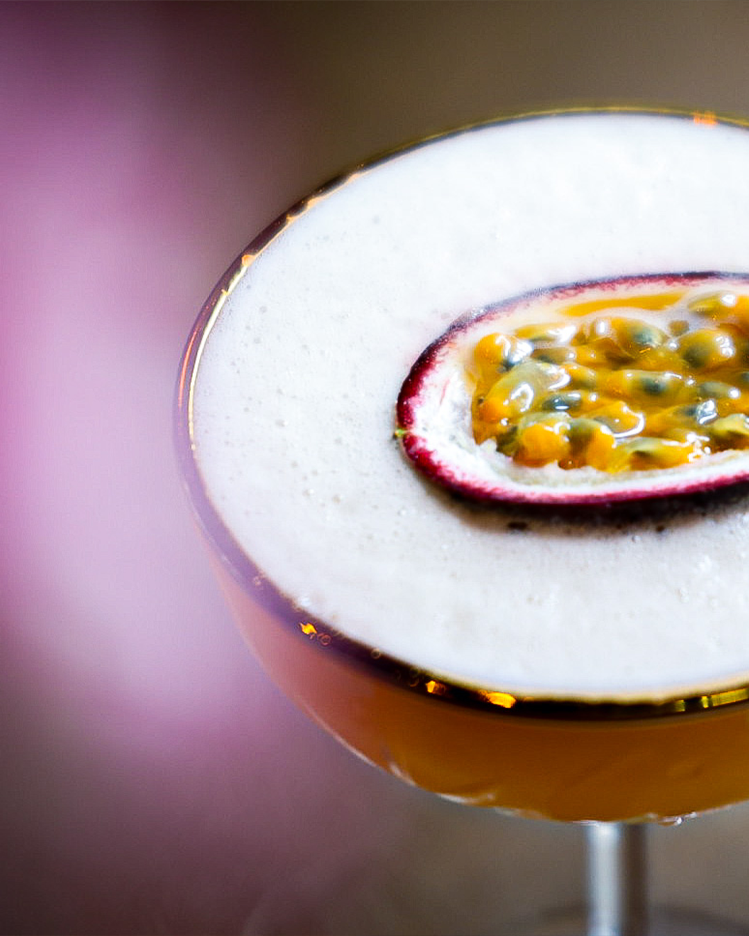 Passievruchtcocktail in een glas op voet, gegarneerd met een halve passievrucht. Schuimlaagje, gouden rand.