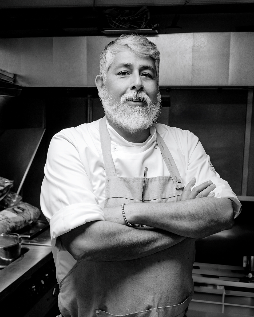 Een chef-kok in een witte koksjas en schort, met de armen over elkaar, in een restaurantkeuken.