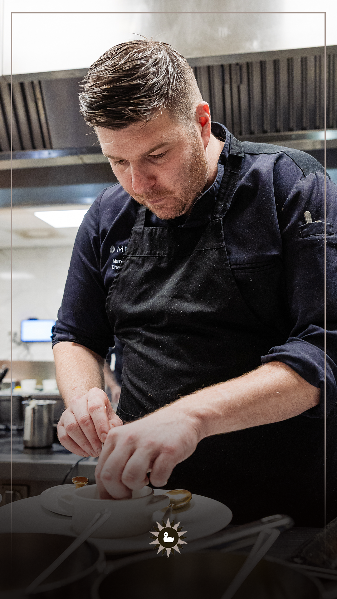 Chef-kok in zwart uniform, bezig met het bereiden van een gerecht in een professionele keuken.