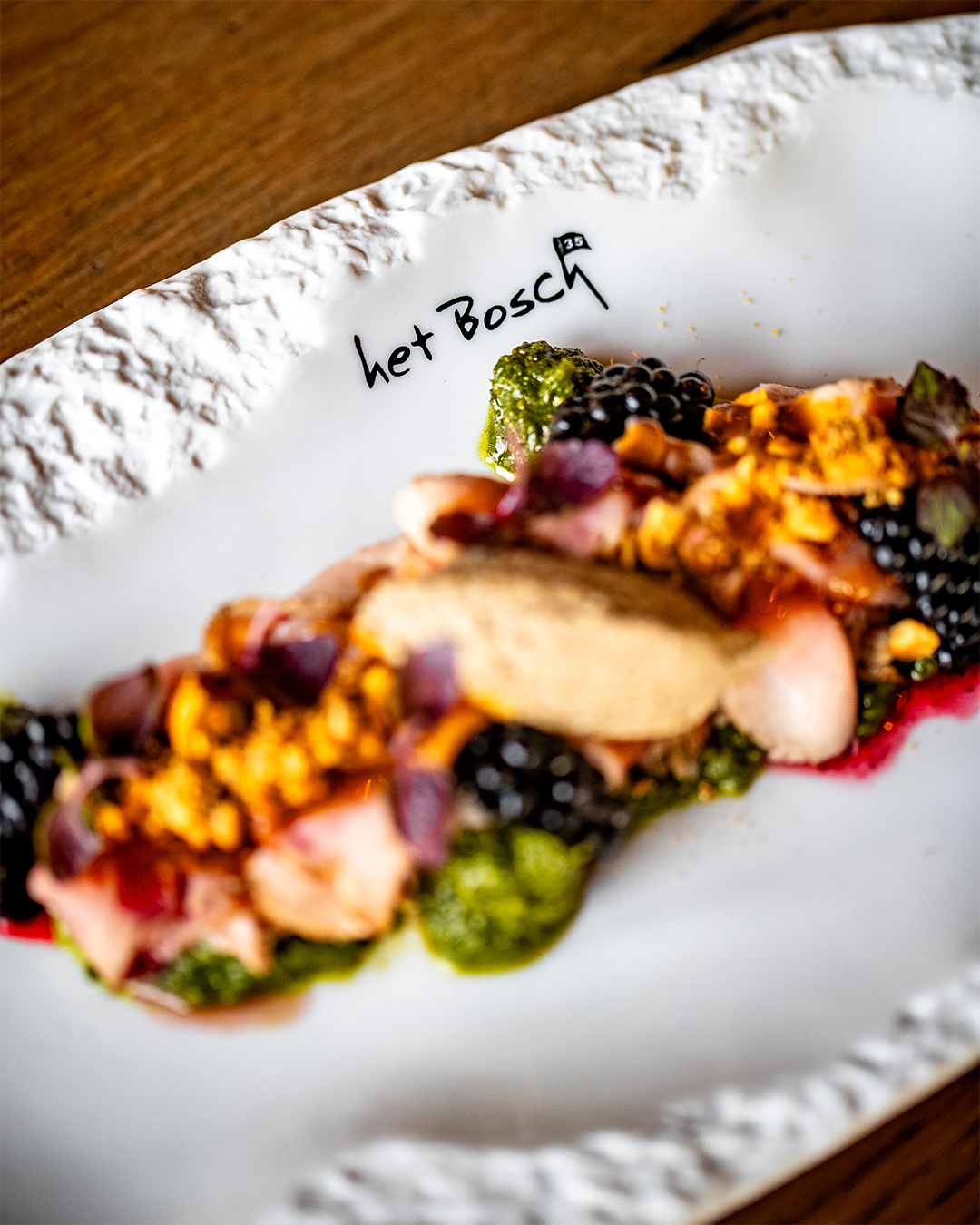 Gerecht op een wit, gestructureerd bord, gegarneerd met bramen, saus en gehakte noten; 