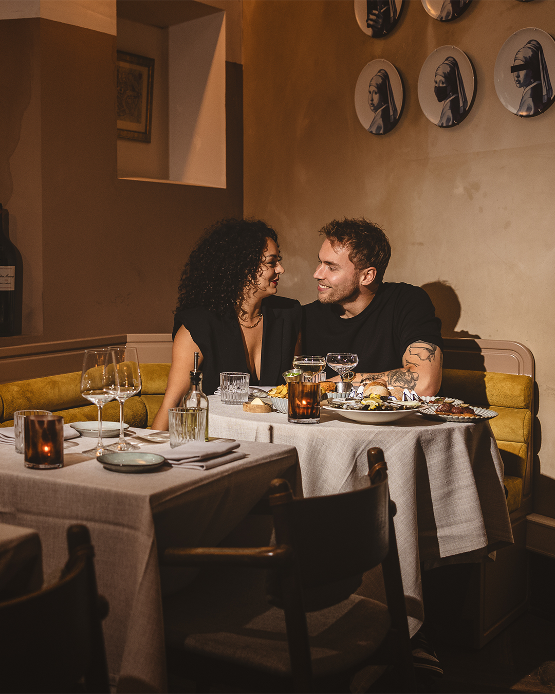 Een stel kijkt elkaar aan aan een restauranttafel. Romantische setting met gedimd licht, lekker eten en wijn.