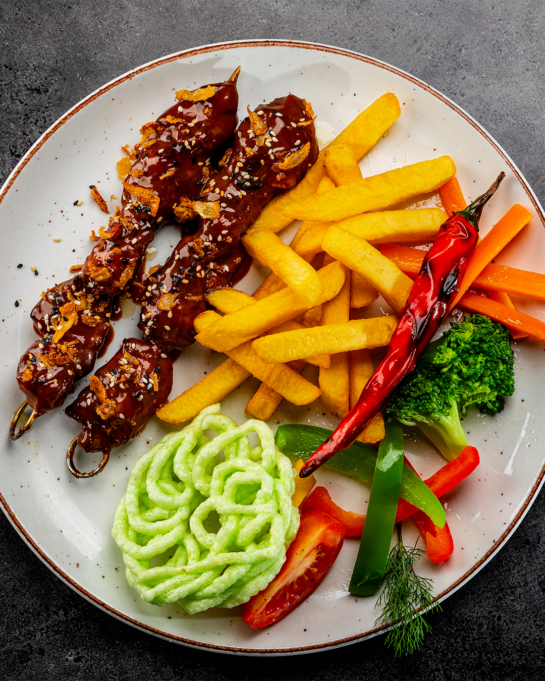 Bord met eten: spiesjes, friet, groenten en een rode paprika.