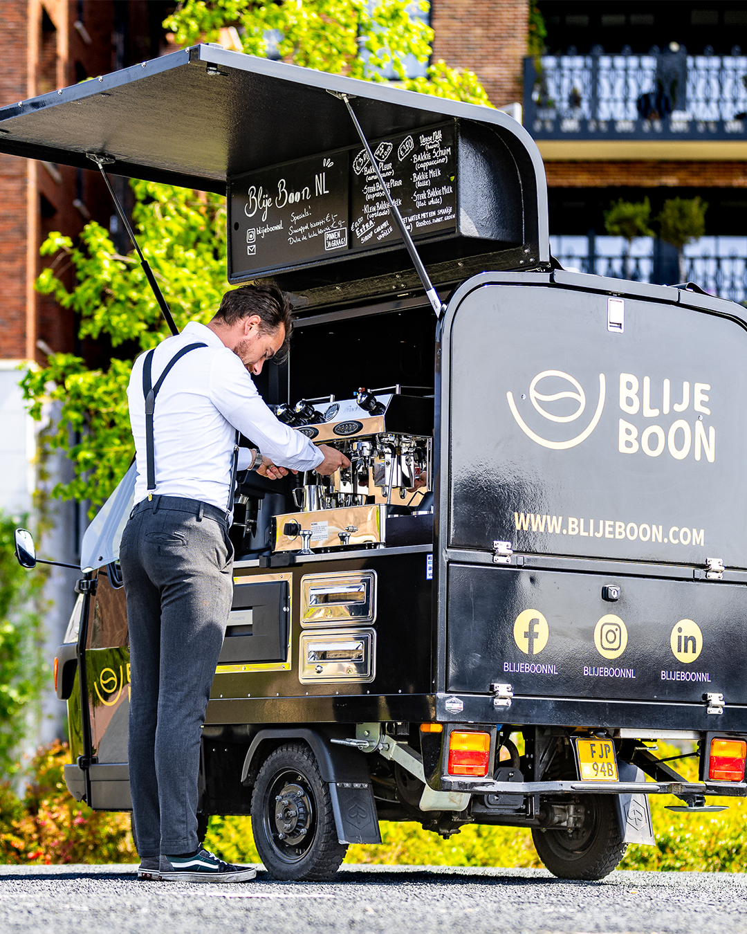 Een man zet koffie bij een zwarte koffiekar met het 