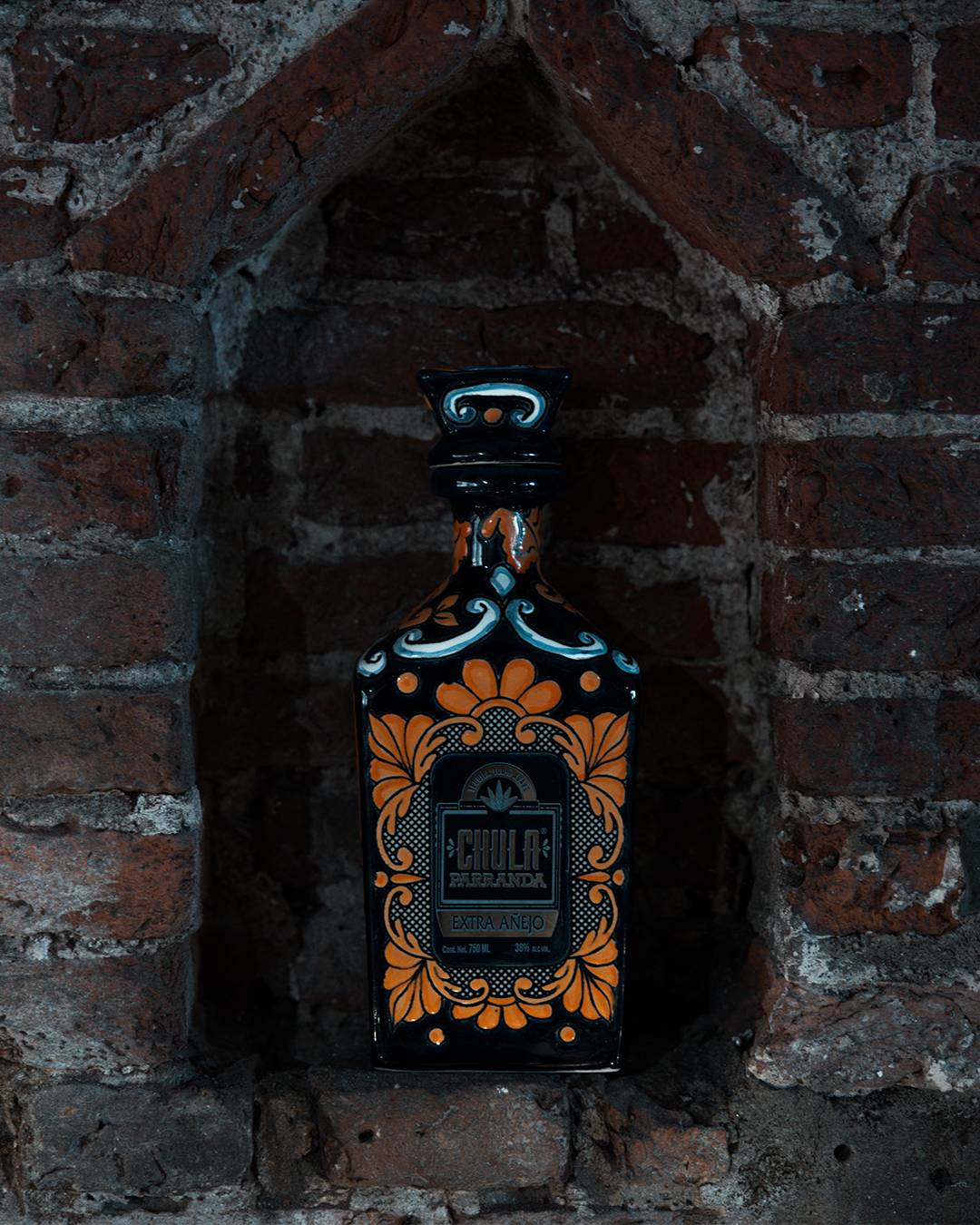 Fles tequila met een oranje en zwart bloemenmotief in een bakstenen nis.